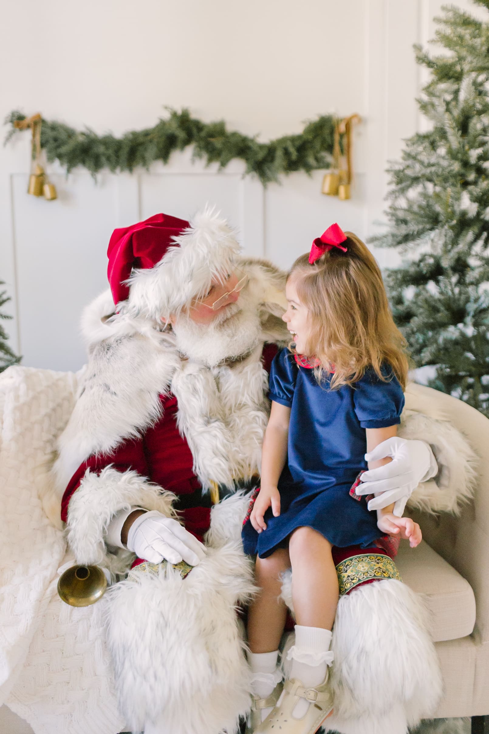A young girl laughs while sitting in the lap of a santa in raleigh in a studio