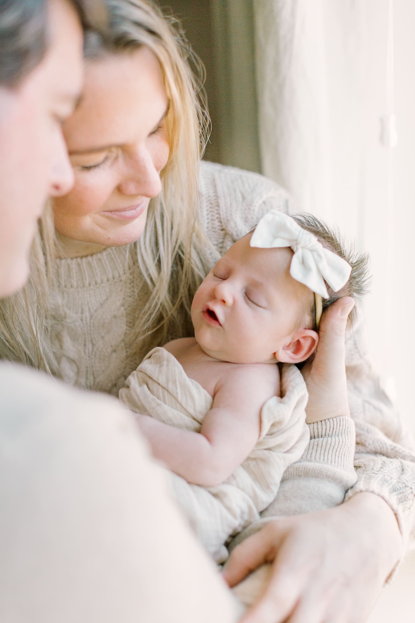 New parents cradle their sleeping newborn daughter in their arms while standing in a window after meeting lactation consultants in Raleigh, NC
