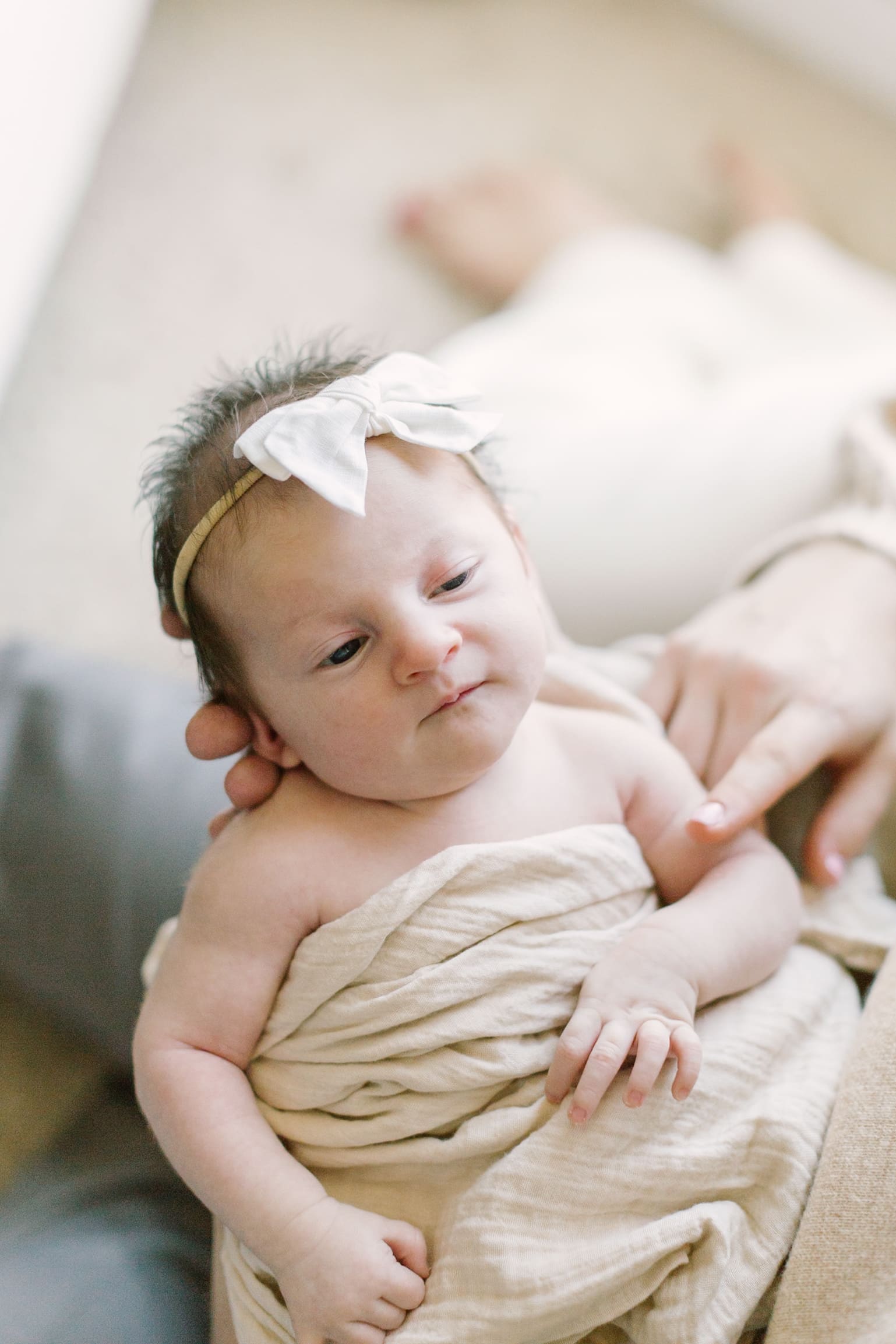 A newborn baby lays in mom's lap wrapped in a tan blanket with a white bow on her head after meeting lactation consultants in Raleigh, NC