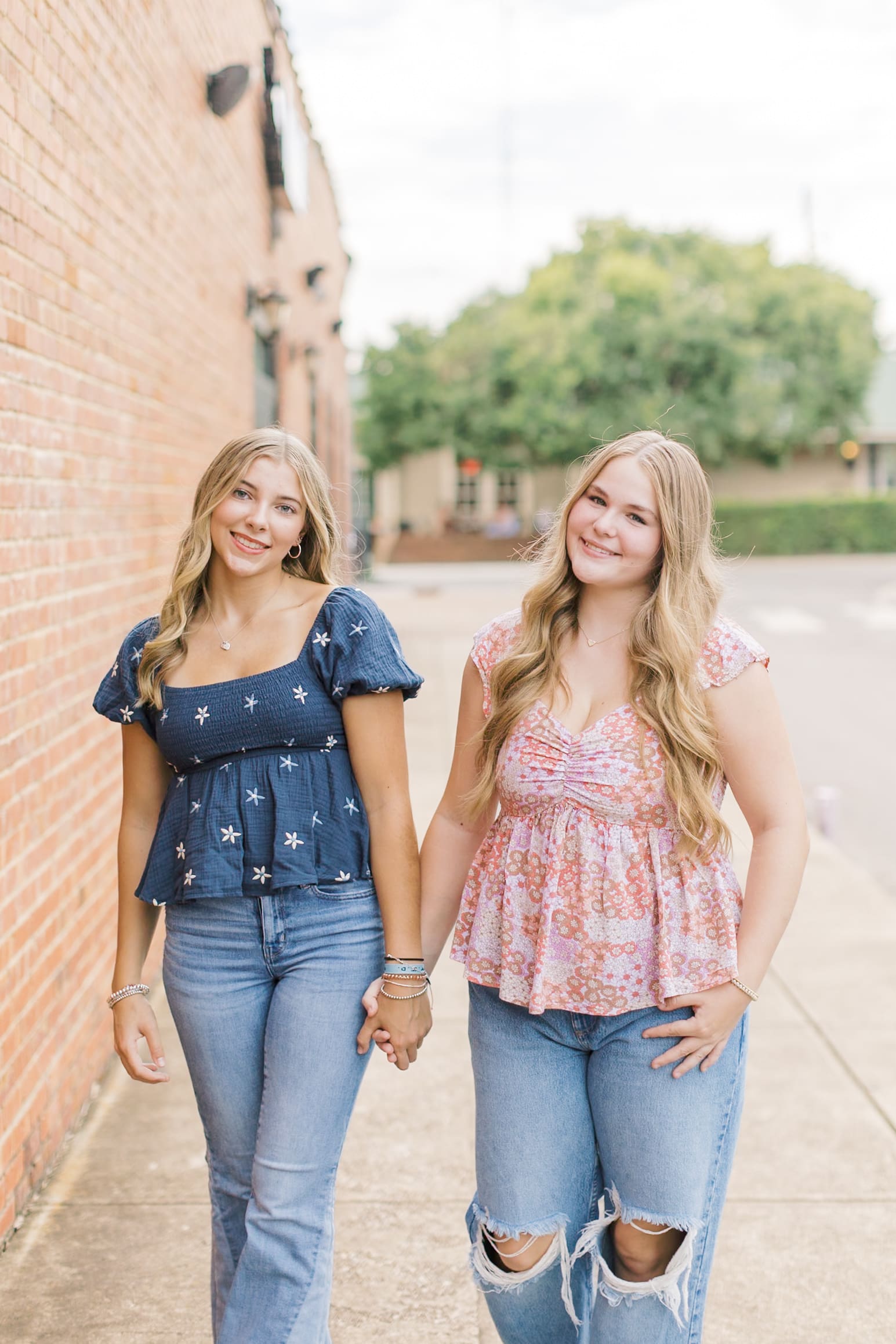 High school senior best friends walk hand in hand down a sidewalk in pink and blue blouses after some Raleigh SAT prep