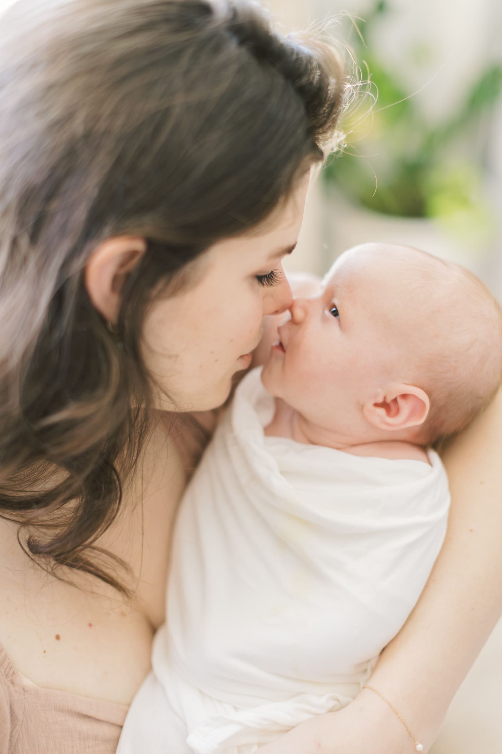 An awake newborn in a white swaddle boops noses with mom after visiting Raleigh baby stores