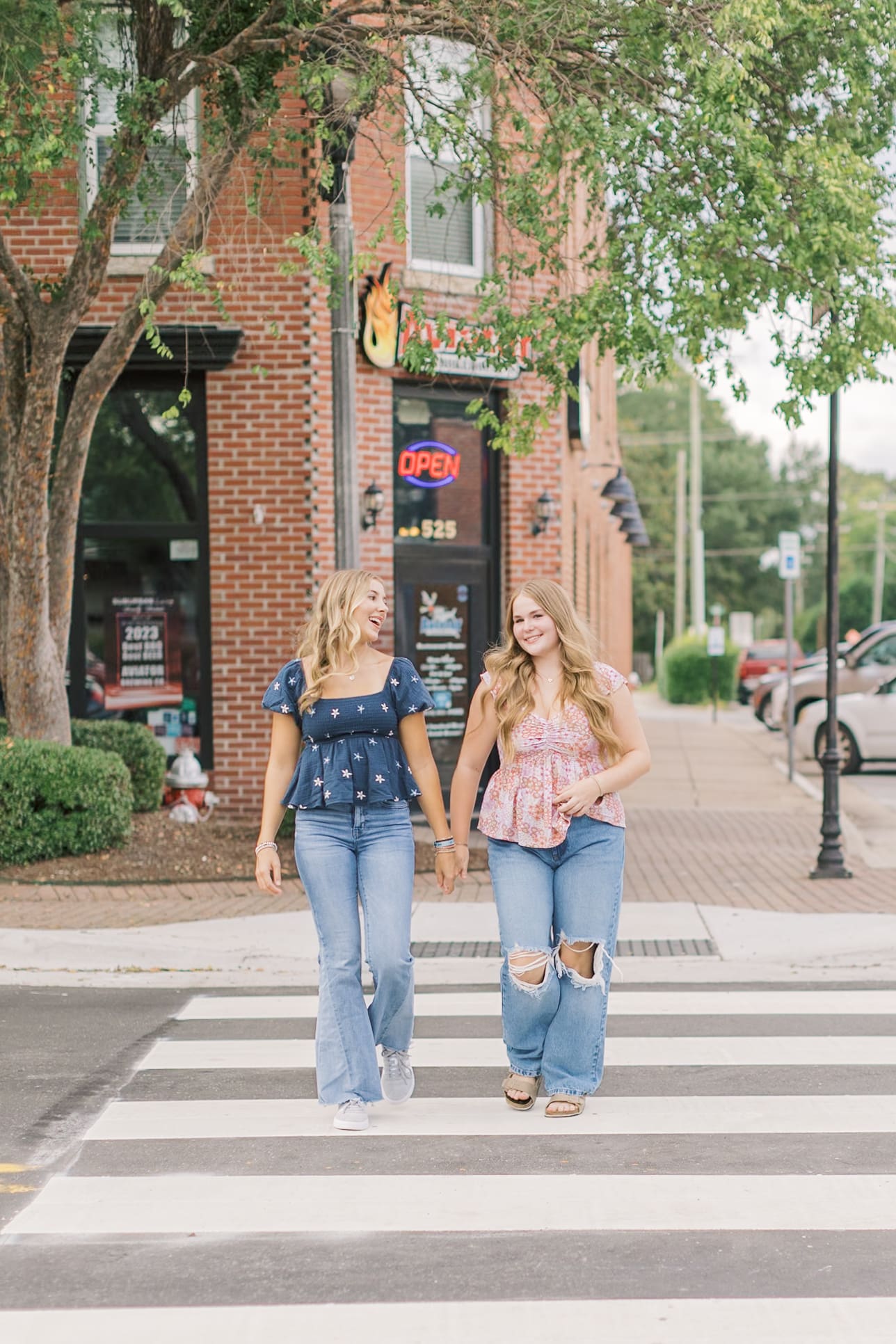 Best friends laugh and walk the crosswalk in downtown in jeans and blue and pink blouses