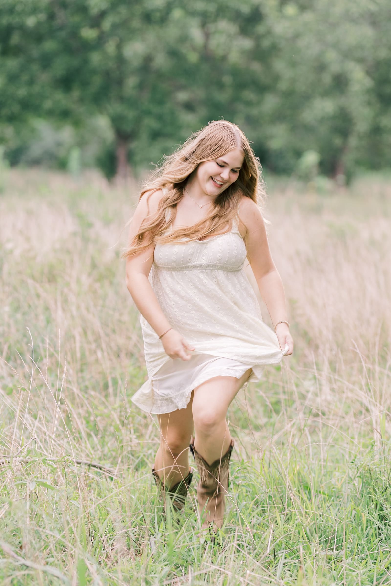 A happy high school senior walks in a pasture of tall golden grass playing with her white dress from Raleigh boutiques