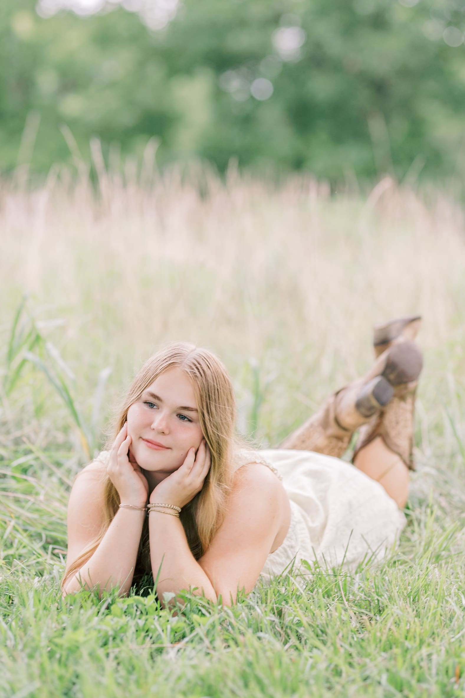 A high school senior in a white dress lays in the grass with her chin in her hands after visiting raleigh hair salons