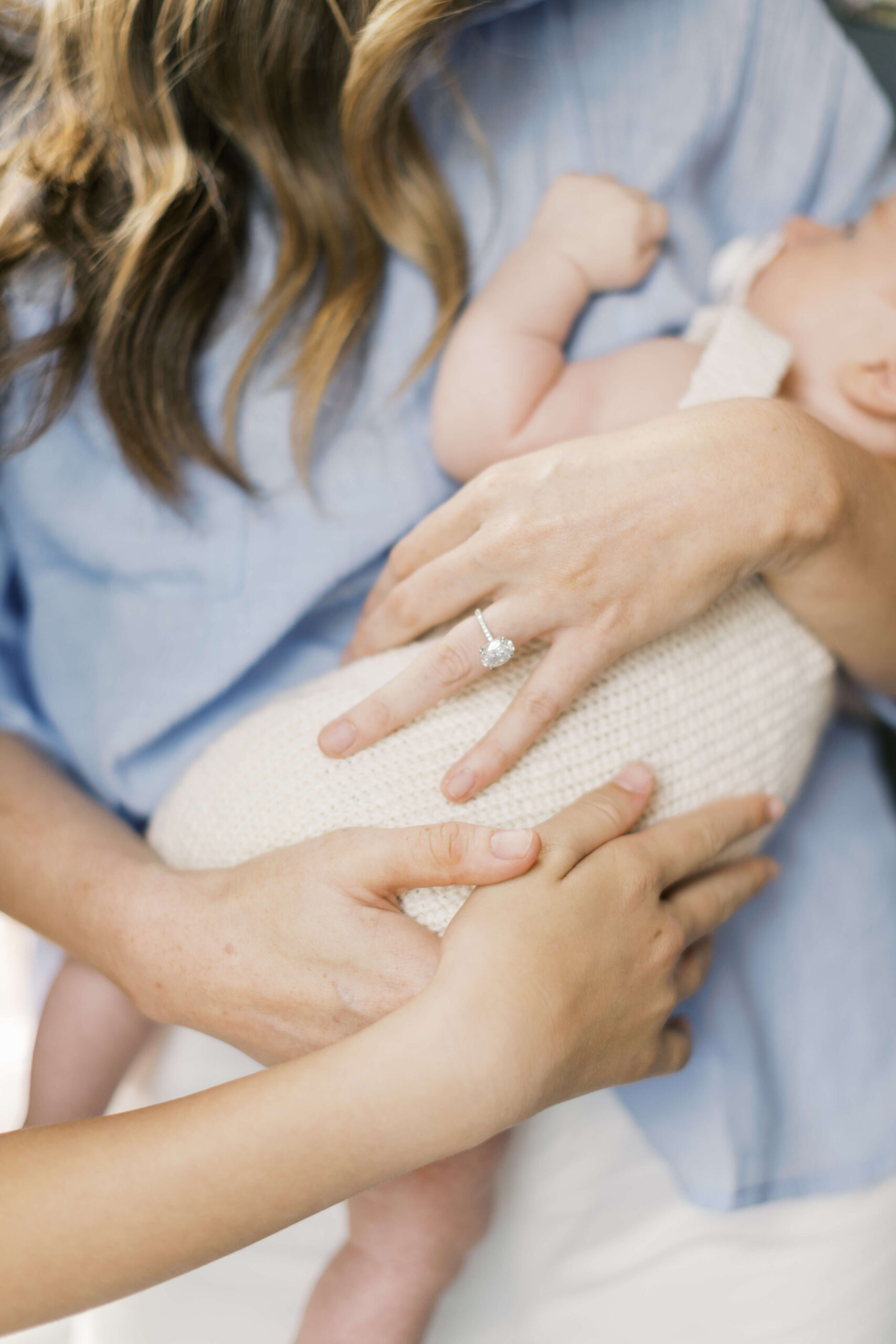 Details of a family of children touching their newborn sibling in mom's arms