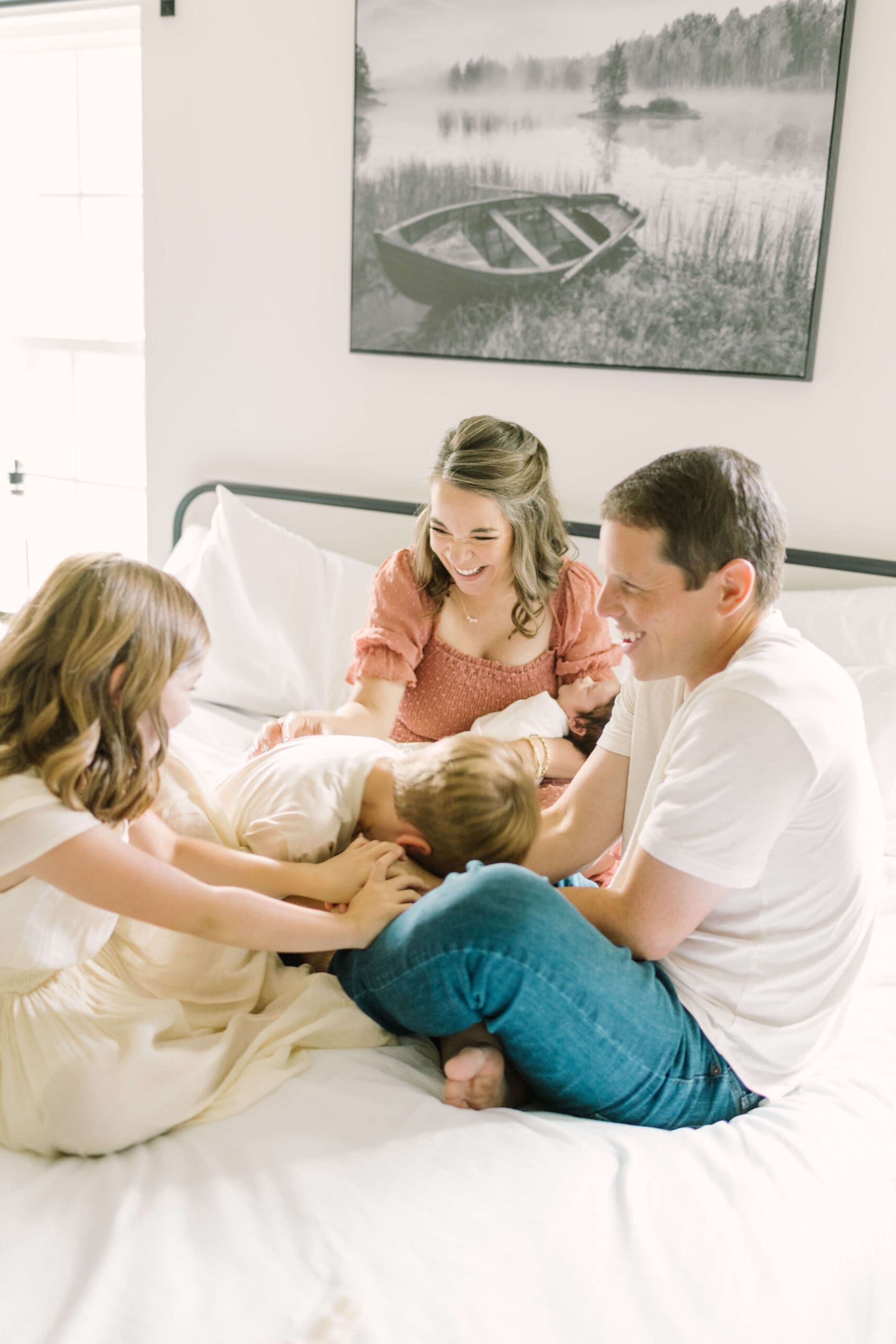 a family of 5 gathers together on a bed laughing together