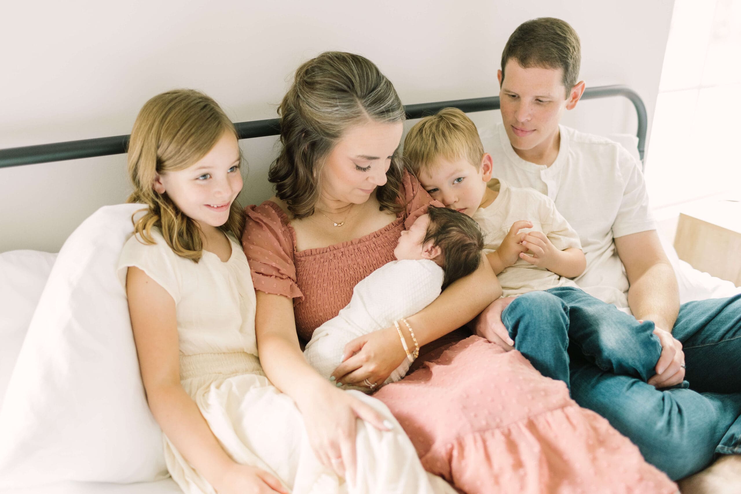 a family of 5 sits together on a bed admiring the newest member of their family after she was born with the help of raleigh doulas