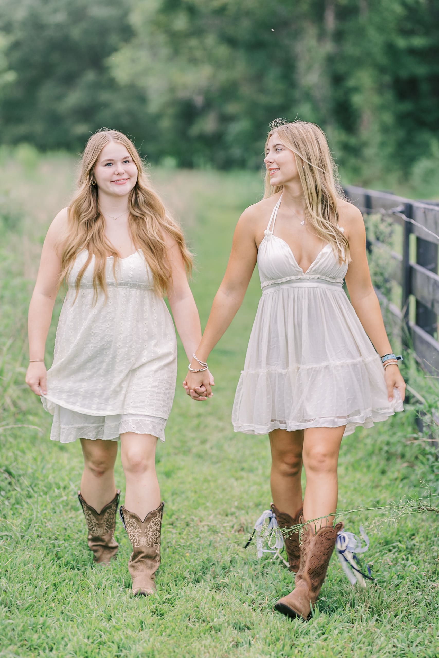High school seniors walk hand in hand near a pasture fence in white dresses and cowboy boots after some Raleigh SAT prep