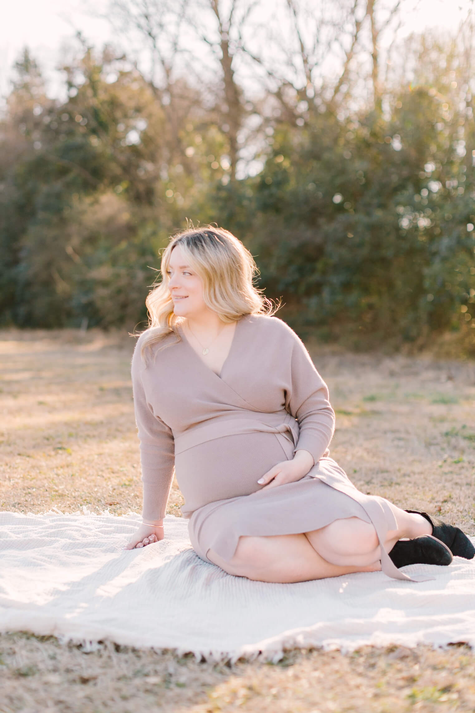 A mother to be smiles while on a picnic blanket in a park at sunset after her 3d ultrasound in raleigh
