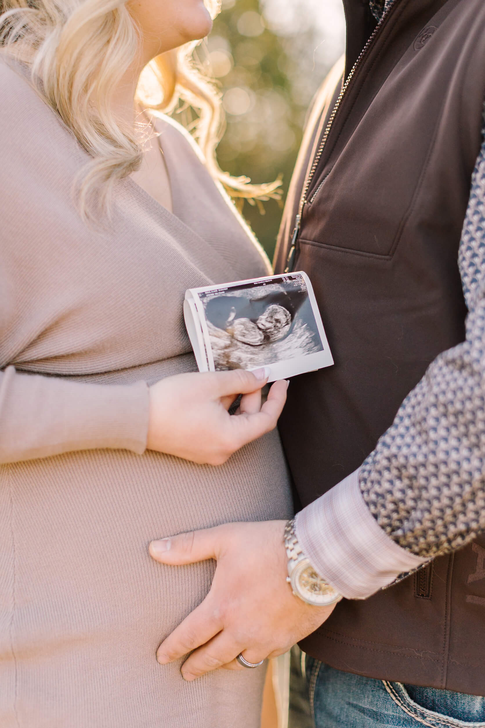 Details of a sonogram being held by a happy mom to be while cuddling her husband at sunset after their 3d ultrasound in raleigh