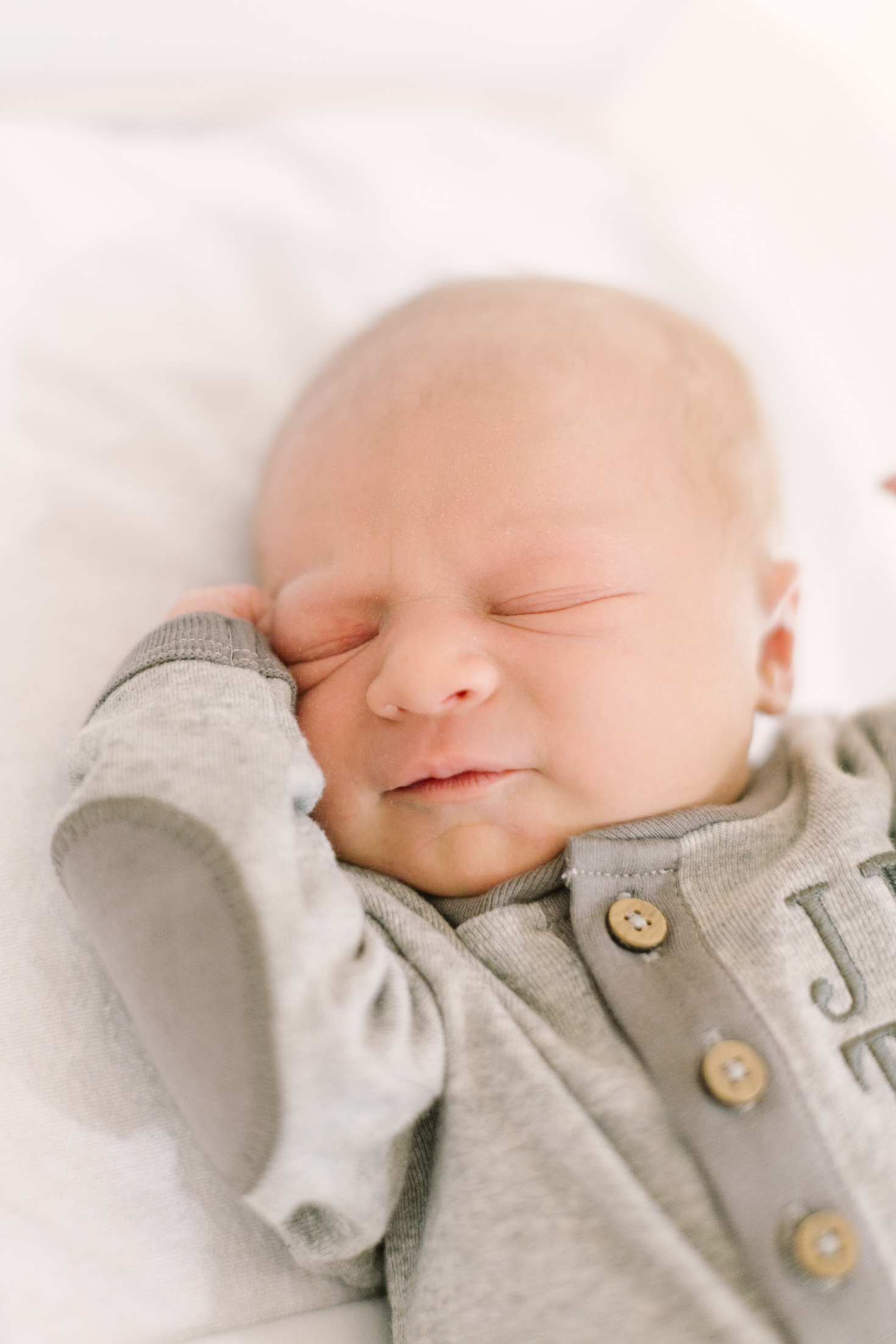 a newborn baby sleeps on a white bed in embroidered onesie