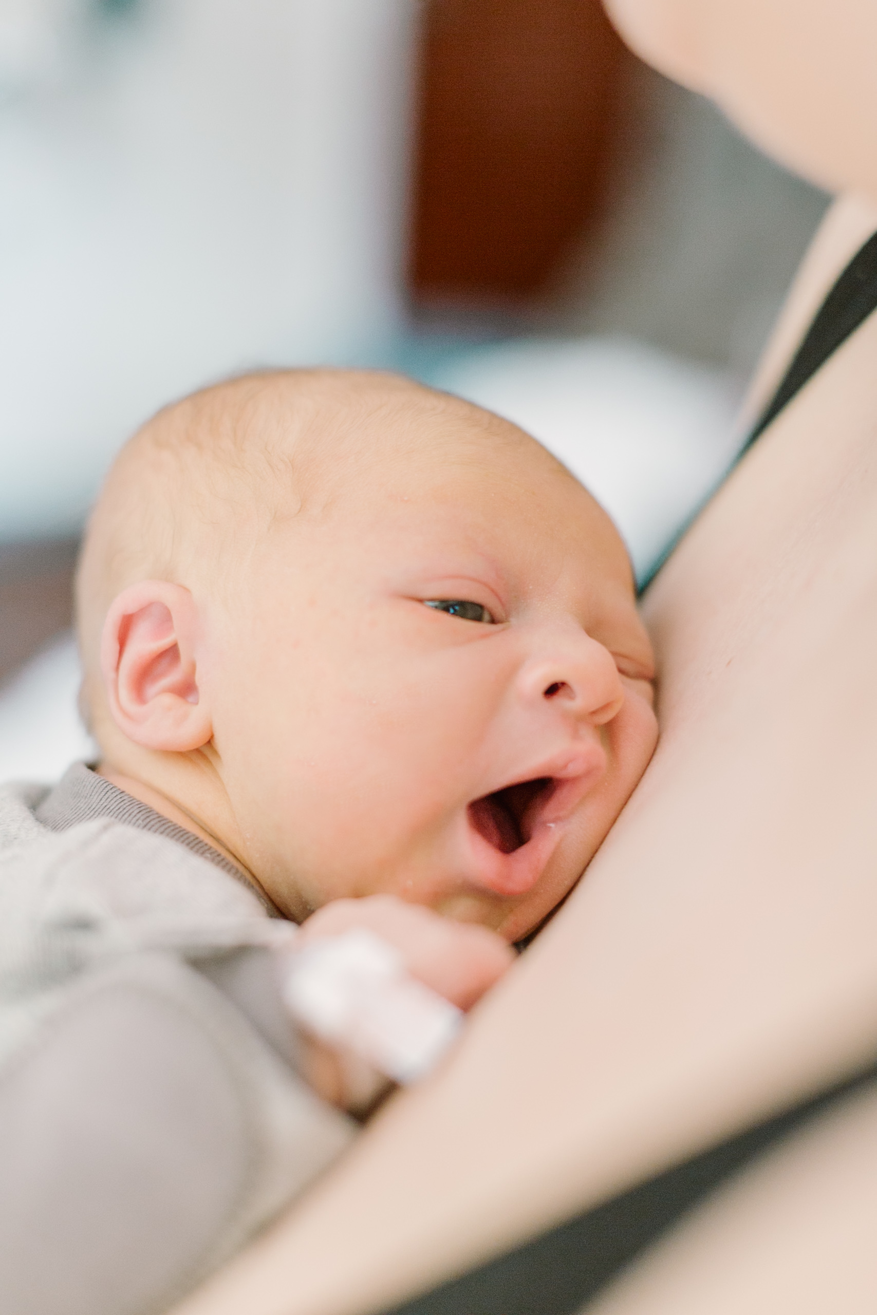 A newborn baby lays against mom's chest with eyes and mouth open