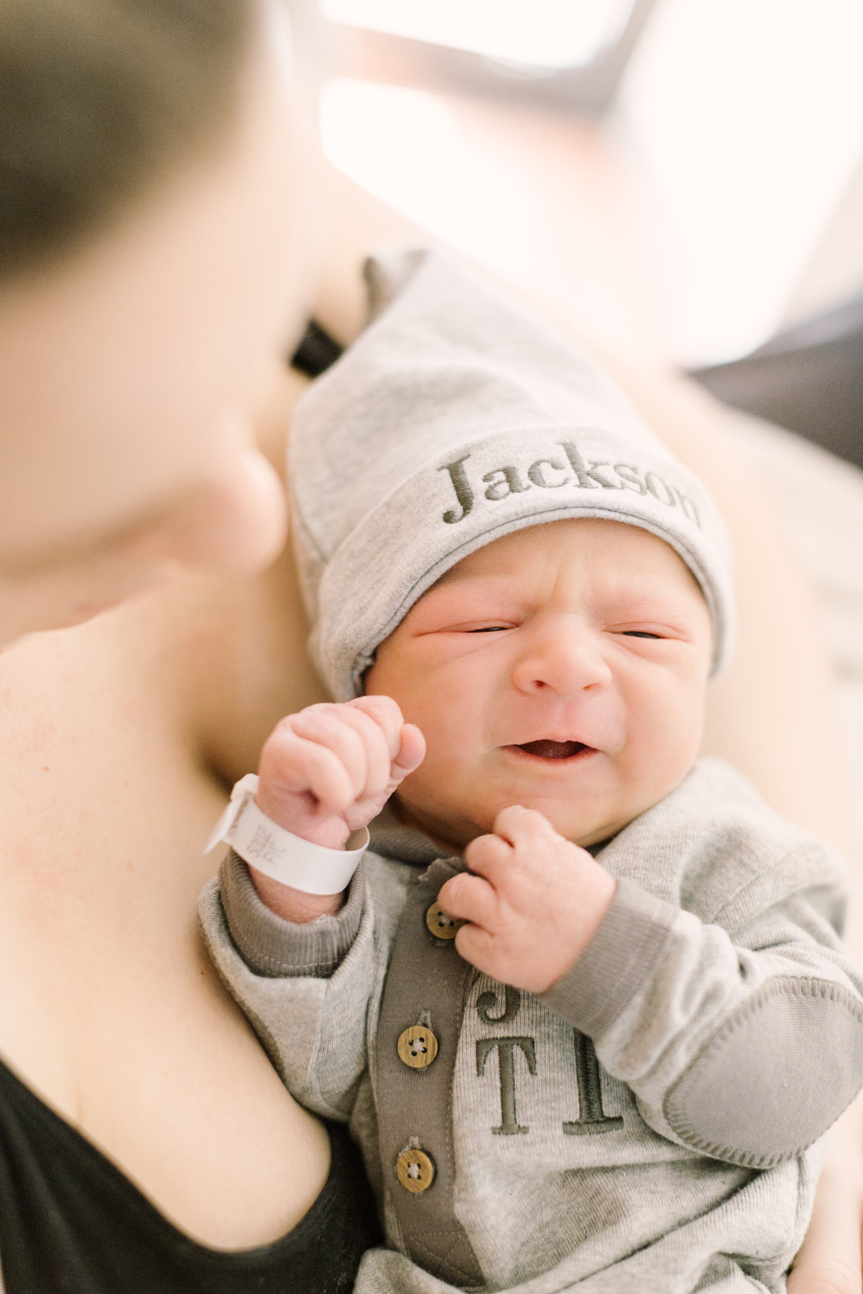 A newborn baby wears a custom sleep cap and matching onesie while laying in mom's chest before finding babysitters in raleigh nc