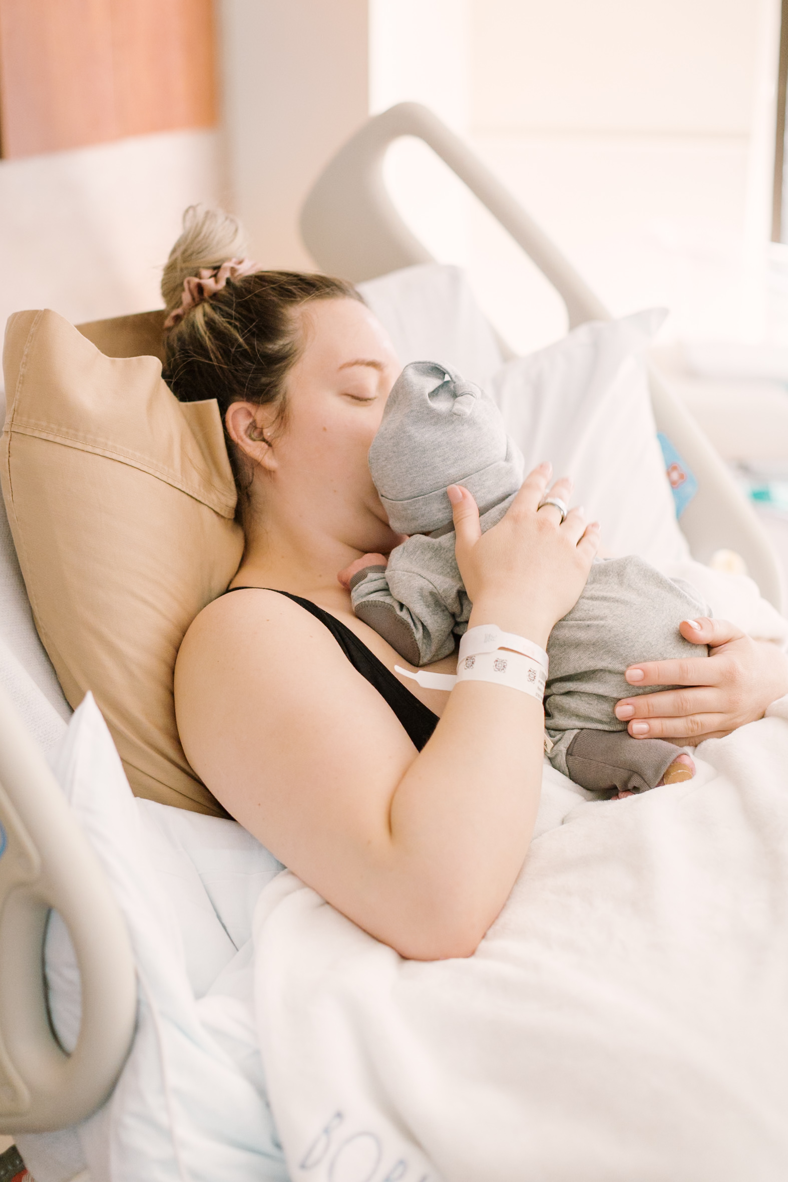 A new mom lays in a hospital bed kissed the head of her newborn laying against her chest before finding babysitters in raleigh nc