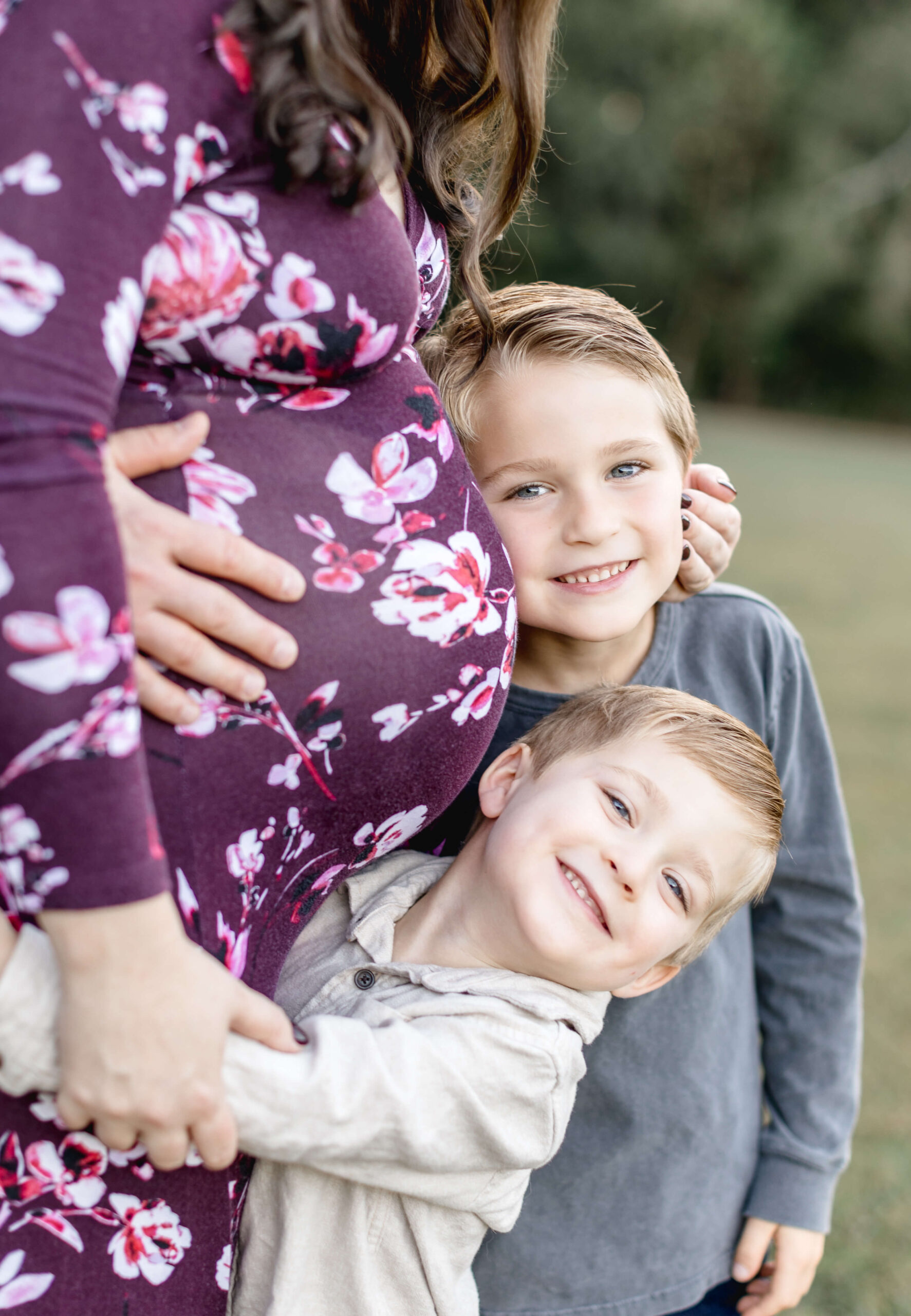 Two young boys in grey and tan shirts hug their pregnant mom while smiling after visiting a birth center in raleigh