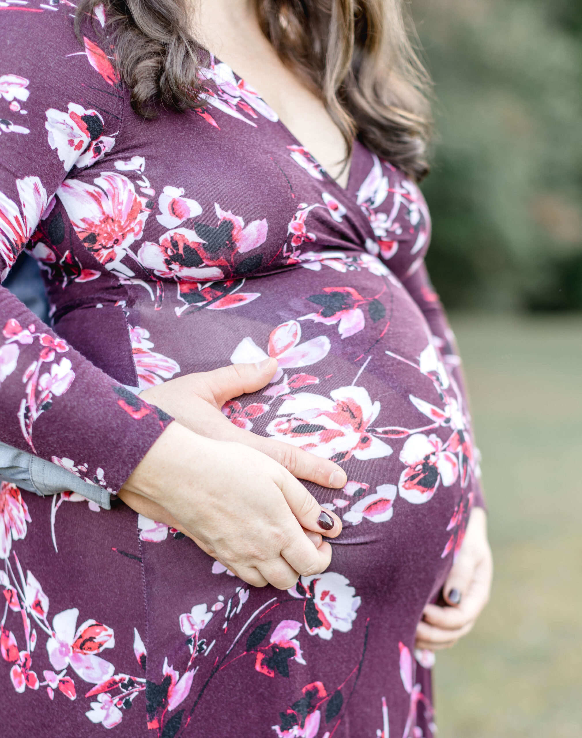 Details of a mom-to-be's bump in a purple floral print maternity gown with hands on it