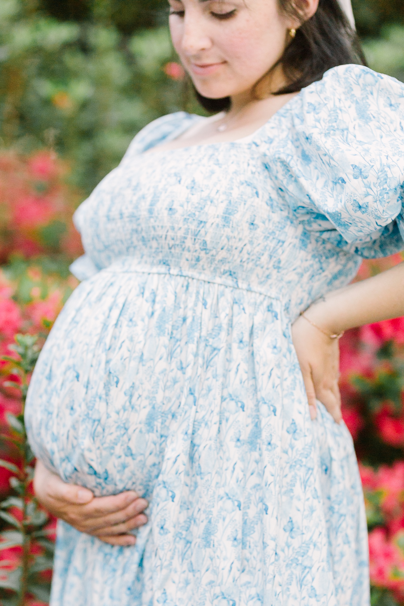 Details of a pregnant woman's hand under her bump in a blue floral print maternity gown thanks to ivf in raleigh