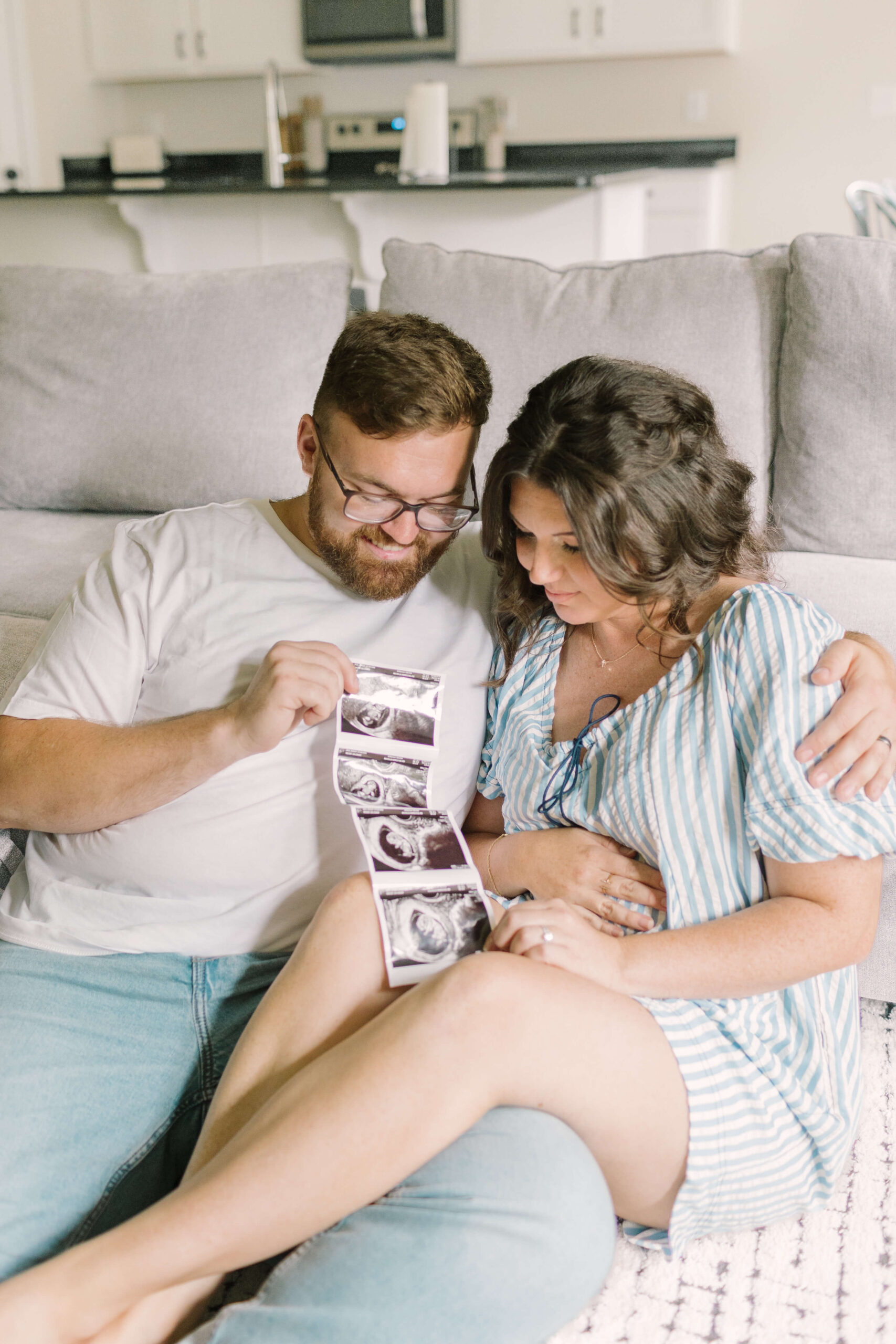 A happy pregnant couple sits against a couch admiring a sonogram after meeting midwives in raleigh