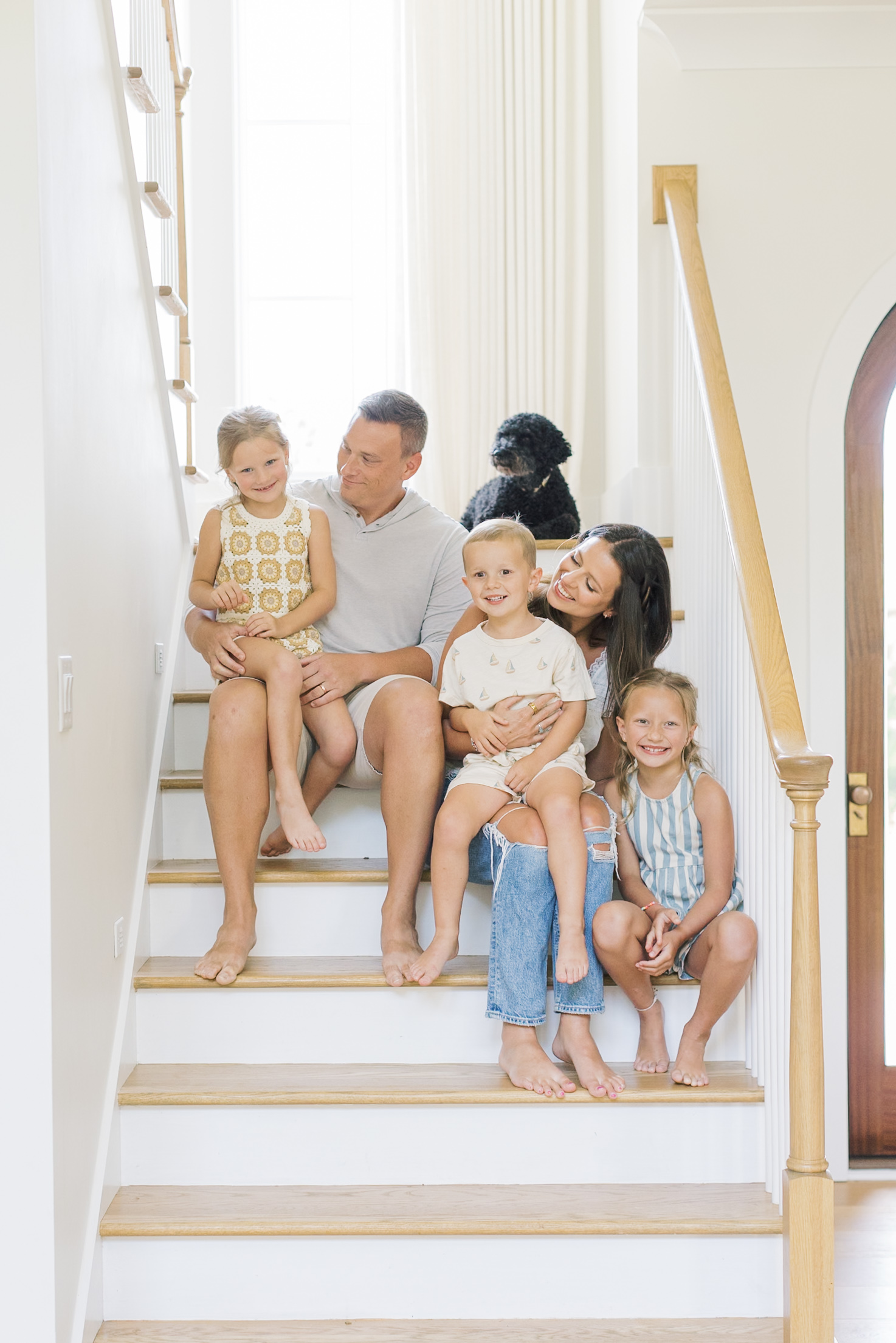 a family of five and their black dog sit on the stairs smiling at each other thanks to parenting classes in raleigh nc