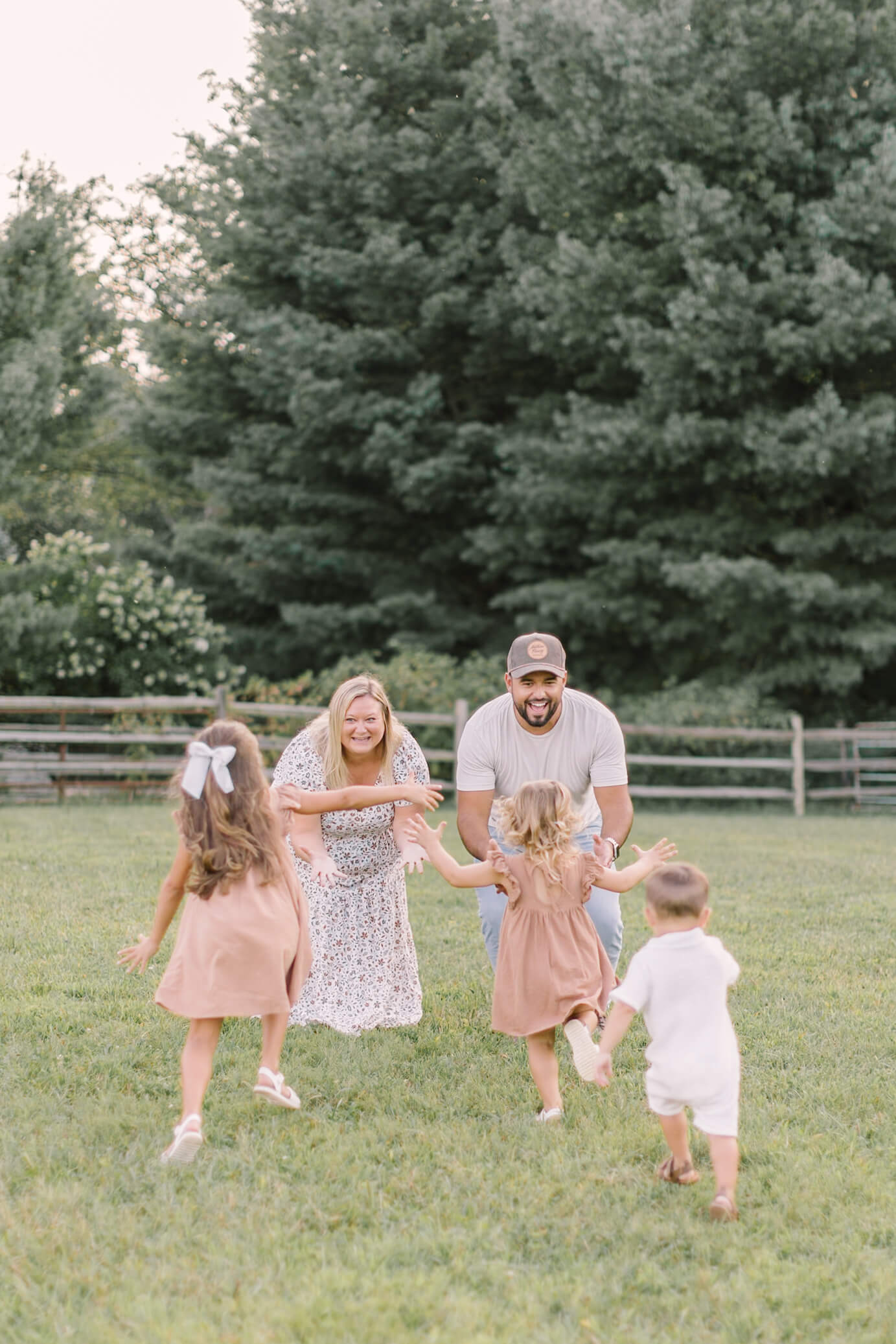 Three toddler siblings run toward mom and dad in a park field at sunset after visiting preschools in raleigh