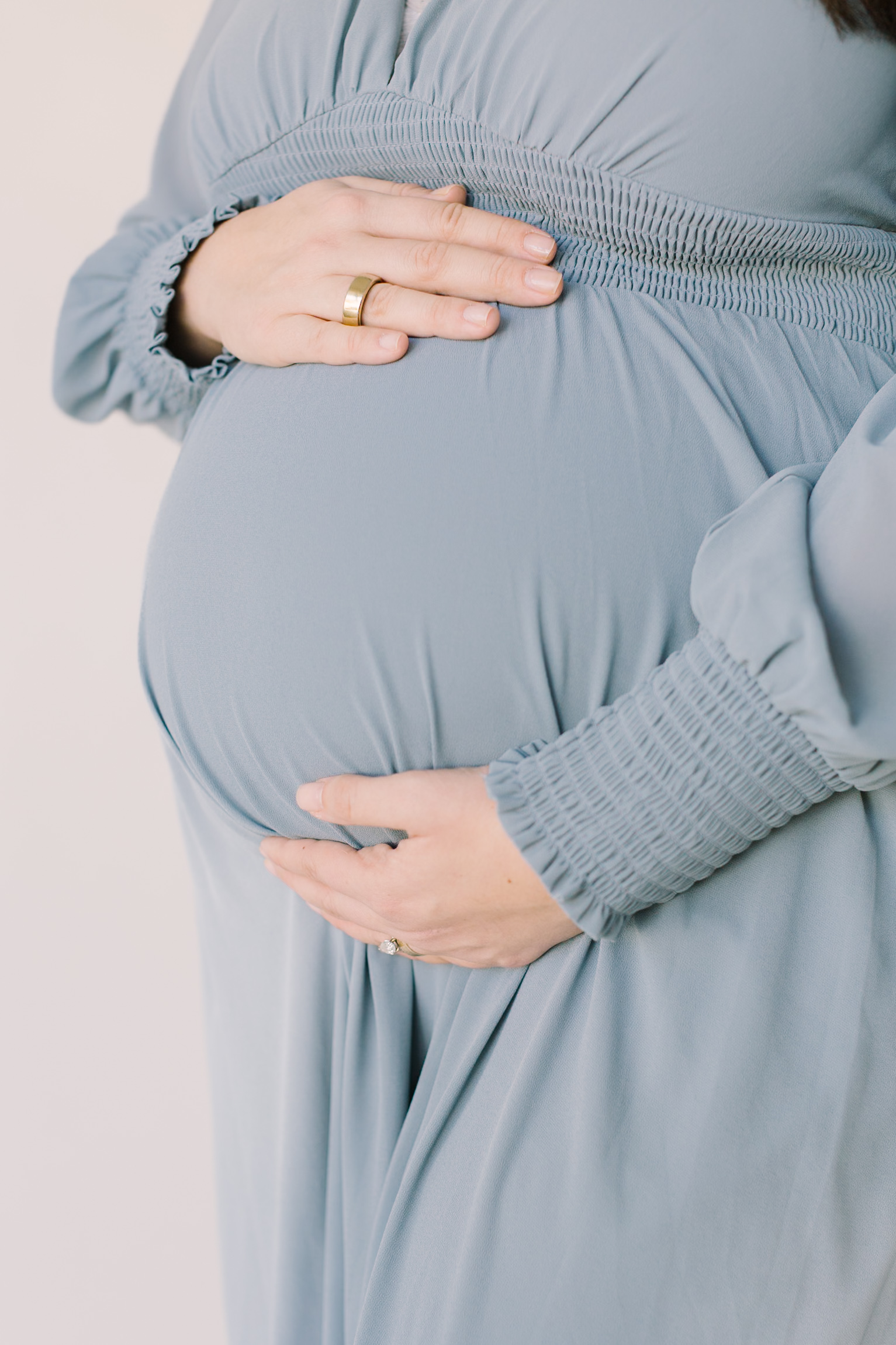 Details of a mother to be standing in a studio holding her bump in a blue maternity gown