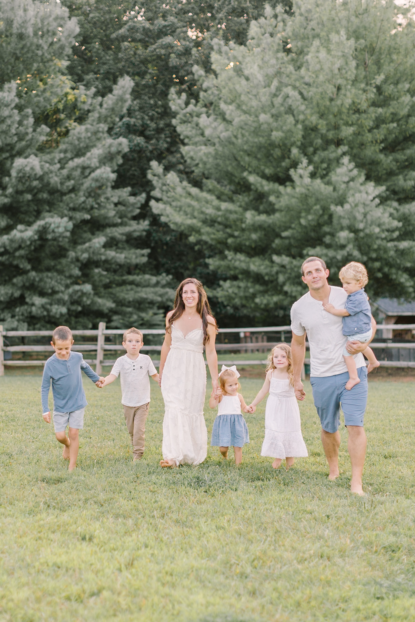 A mom and dad walk holding hands with their 5 children holding hands in a pasture at sunset