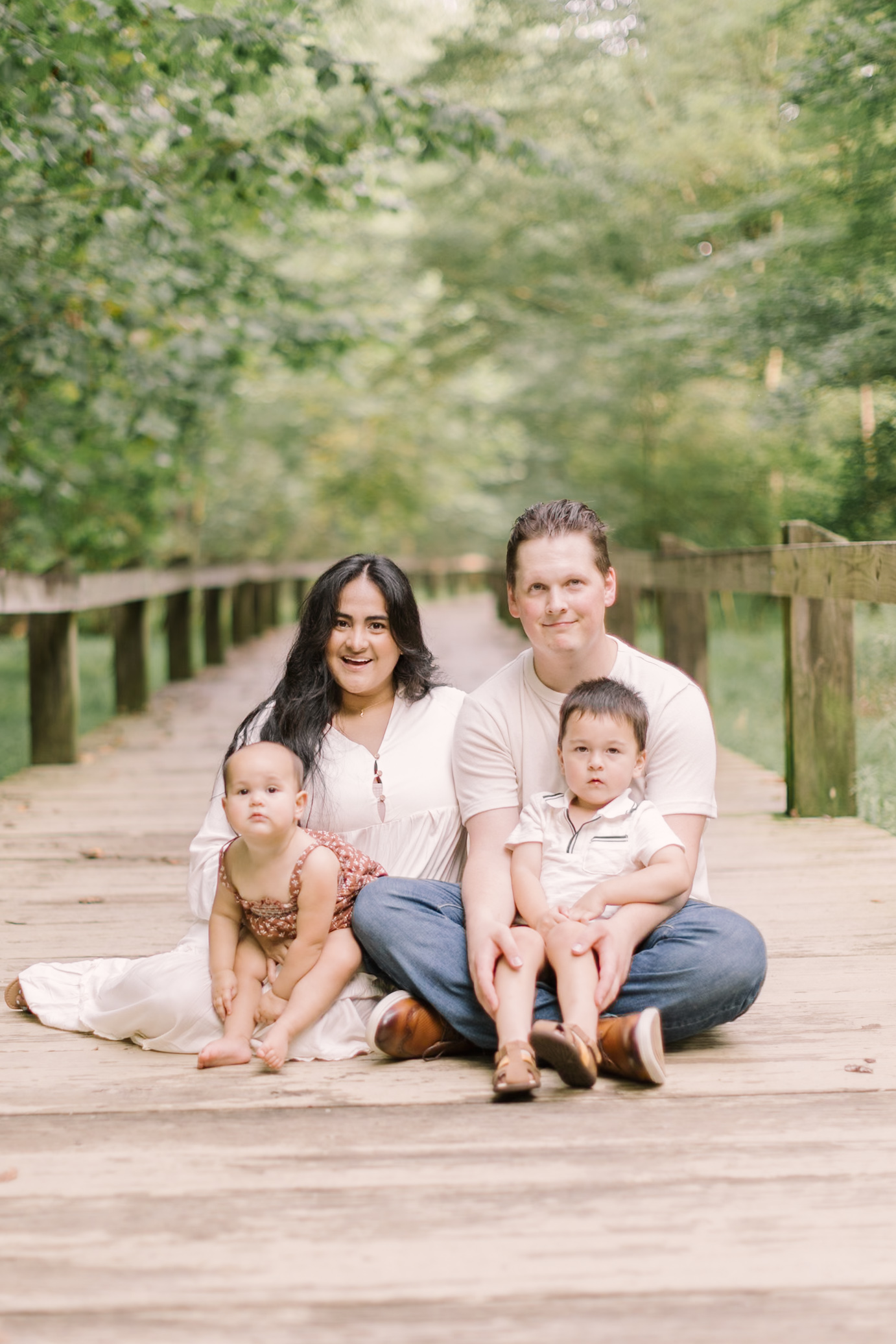 A mom and dad sit on a boardwalk with heir toddler son and daughter in their laps after visiting toy stores in raleigh