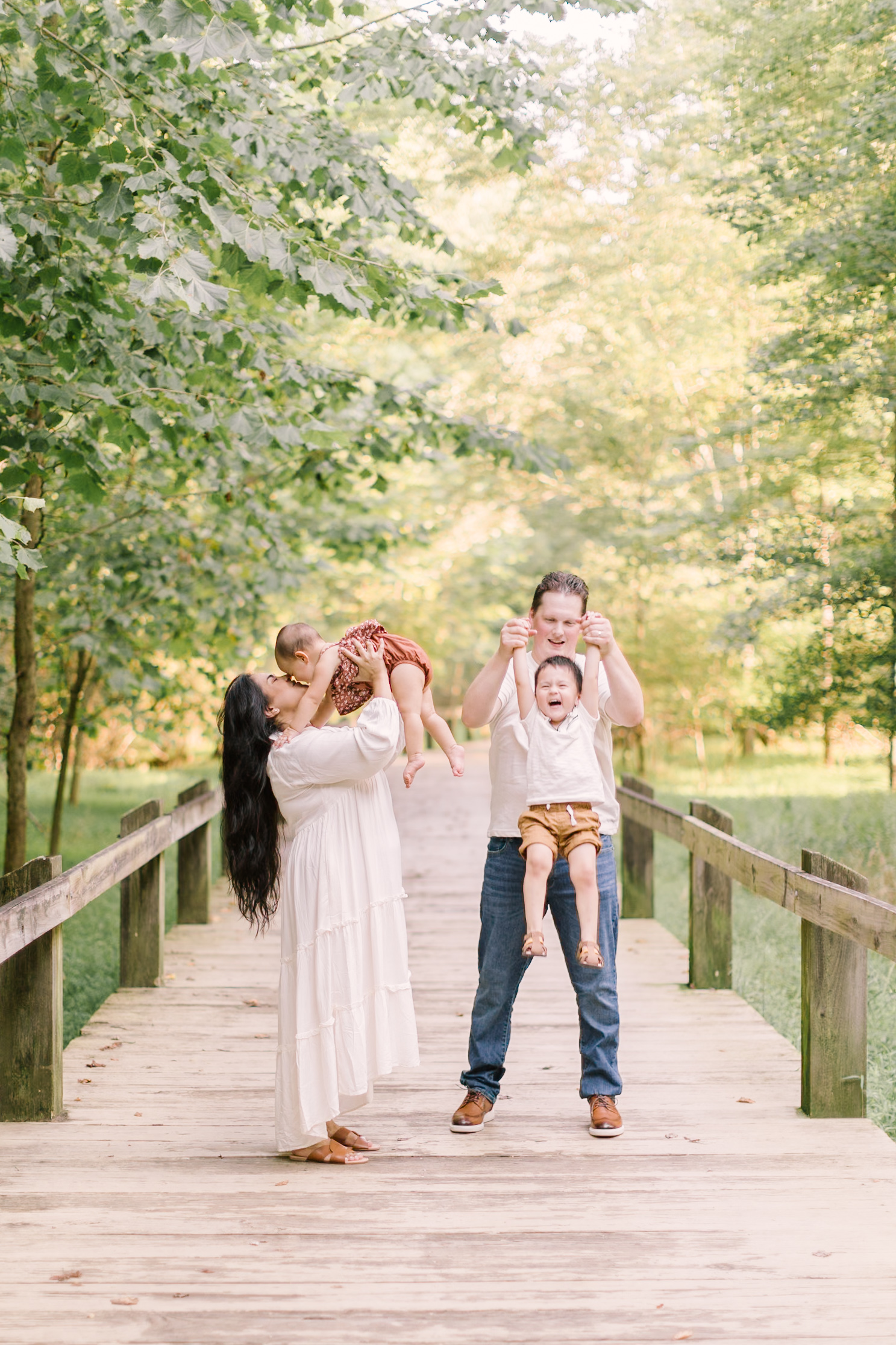 A mom and dad lift and play with their toddler son and daughter on a boardwalk after visiting some toy stores in raleigh