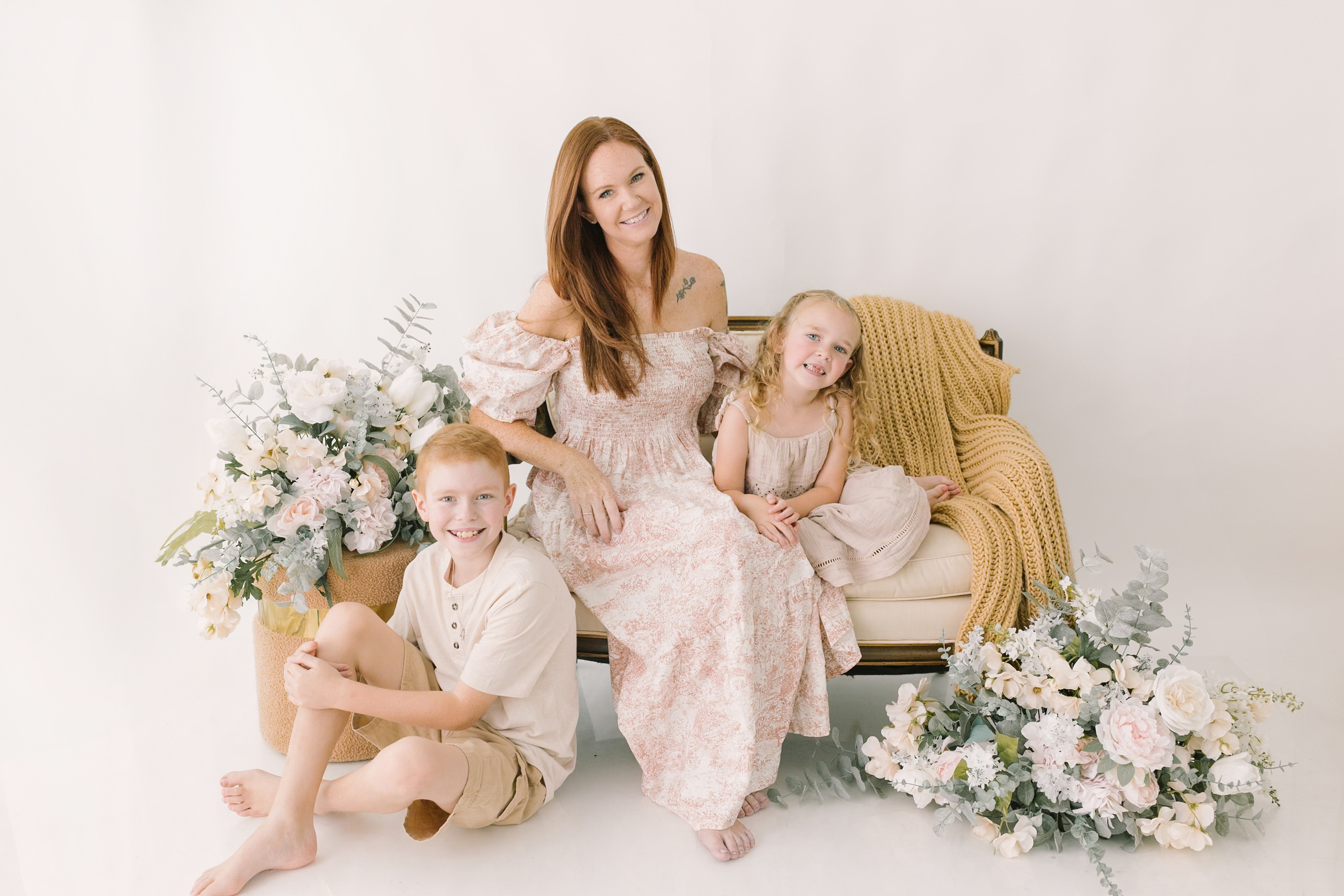 A smiling mom sits on a bench with her toddler son and daughter