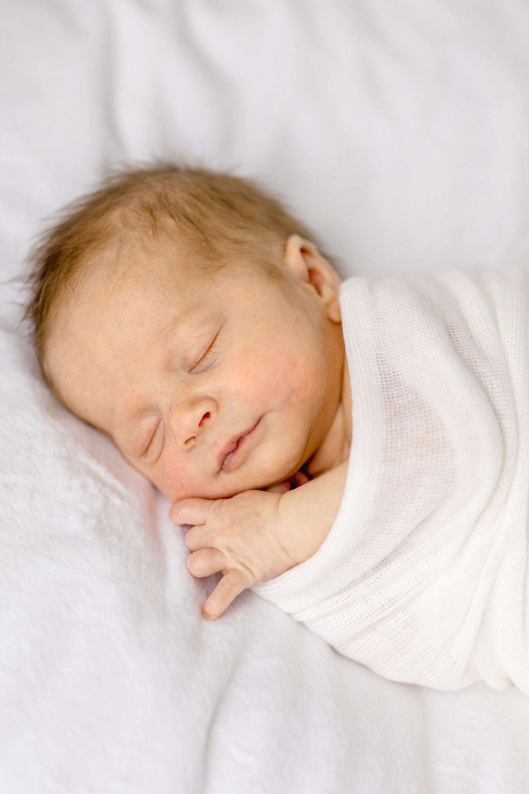 A newborn baby sleeps in a white swaddle on its side on a white bed thanks to pediatric chiropractors in raleigh