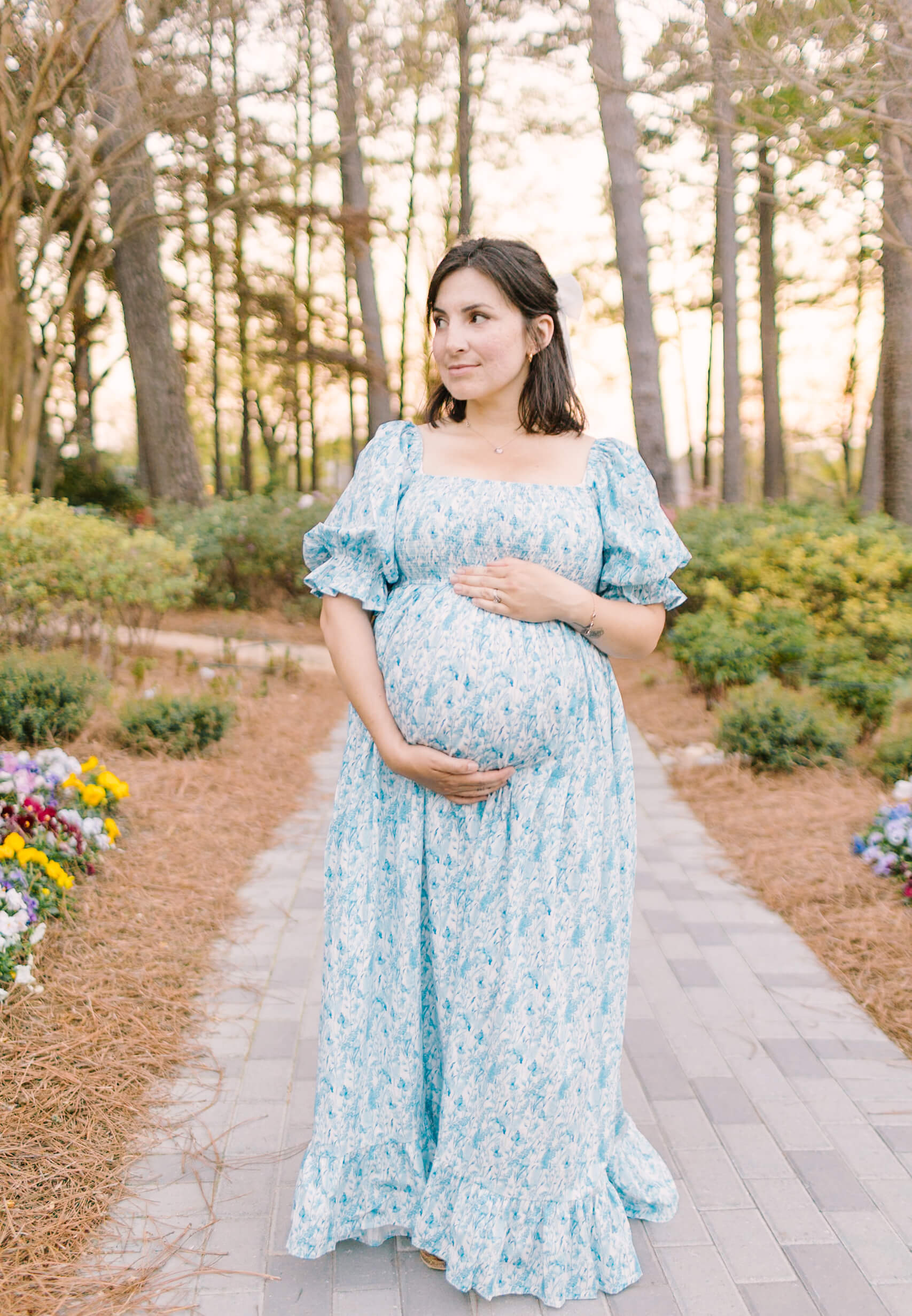 A mother to be smiles while walking a garden at sunset in a blue maternity dress after a prenatal massage in raleigh