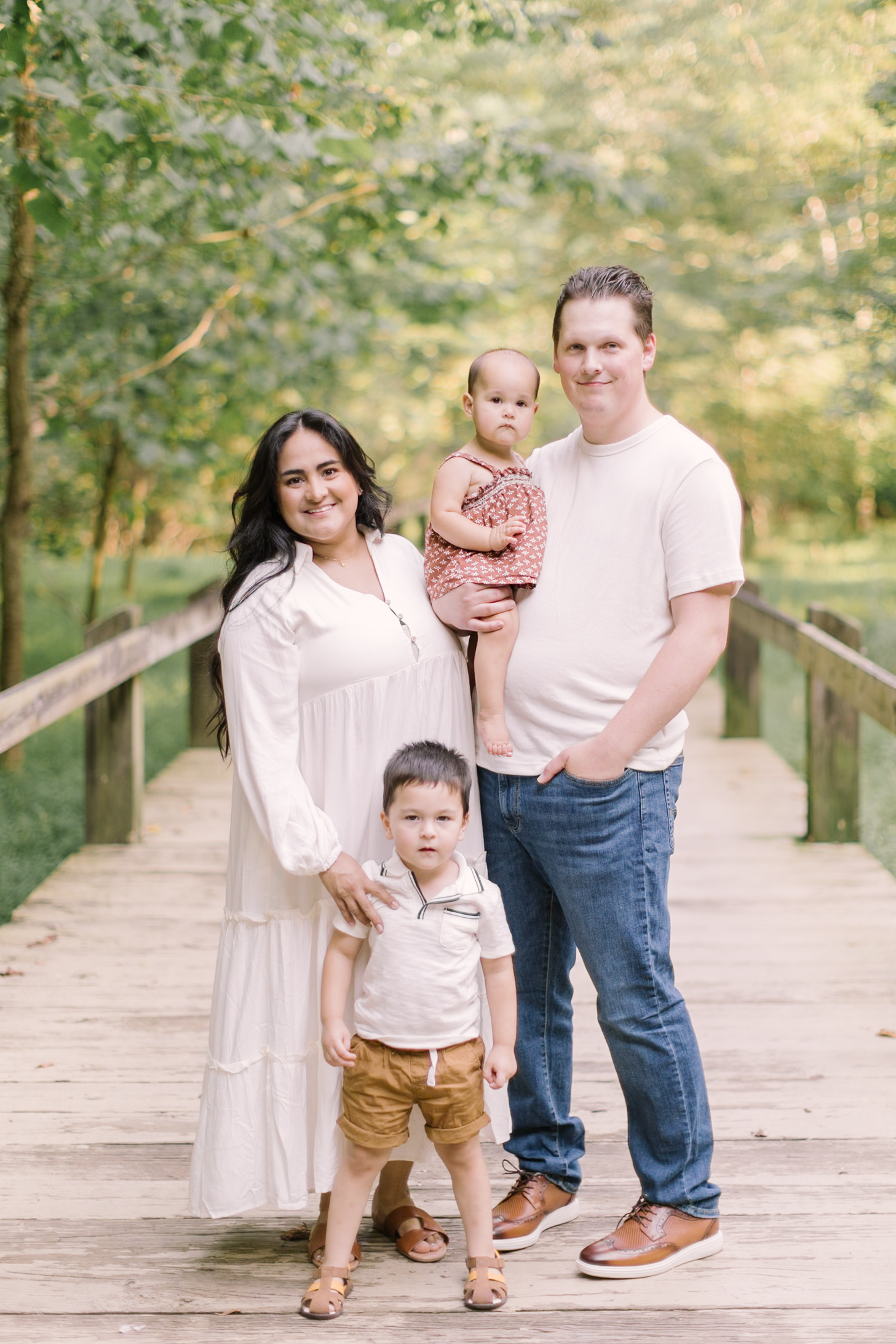 A happy family of four smiling on a boardwalk with two toddlers
