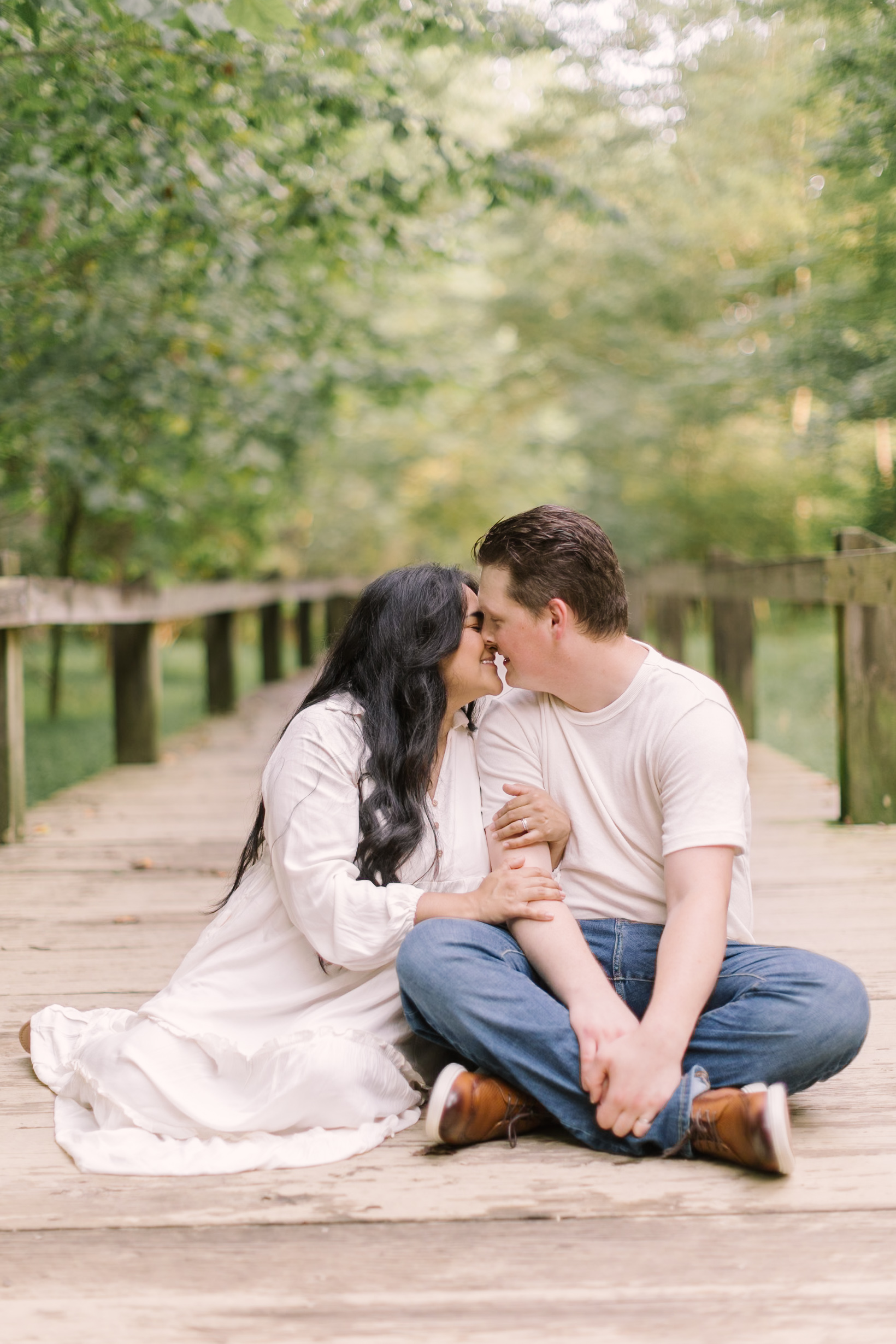 Happy parents sit snuggling and leaning in for a kiss on a boardwalk after Easter brunch in raleigh