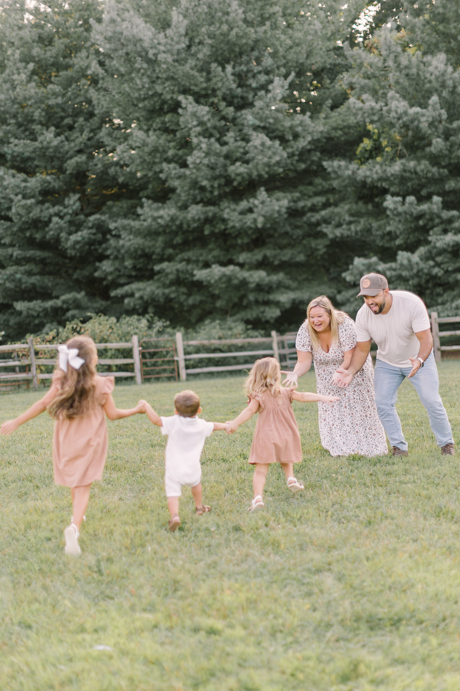 Three toddler siblings in pink and white run towards mom and dad in a park lawn at sunset before heading to easter egg hunts in Raleigh, NC
