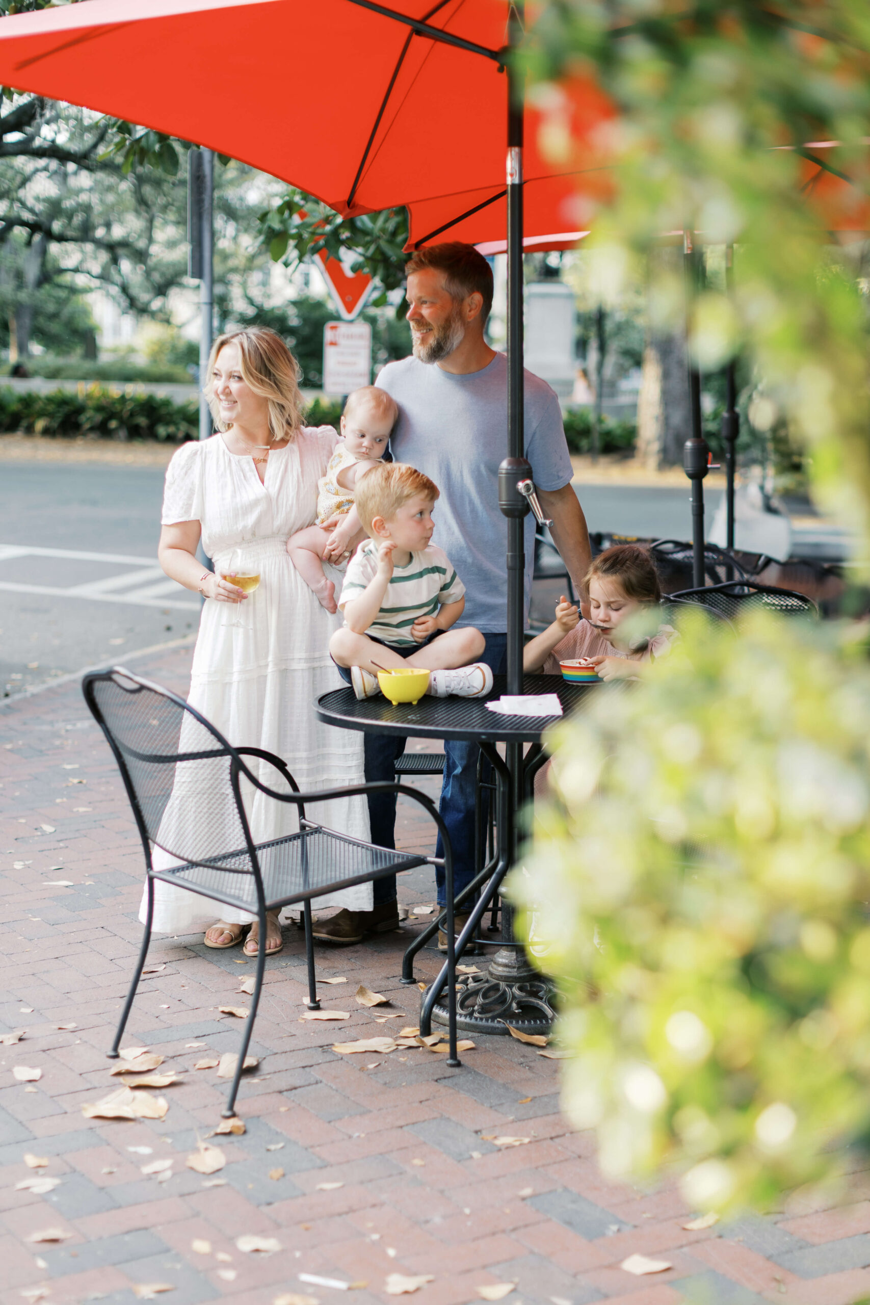 A mom and dad stand under patio umbrellas at one of the family-friendly restaurants in Raleigh, NC with their three toddlers
