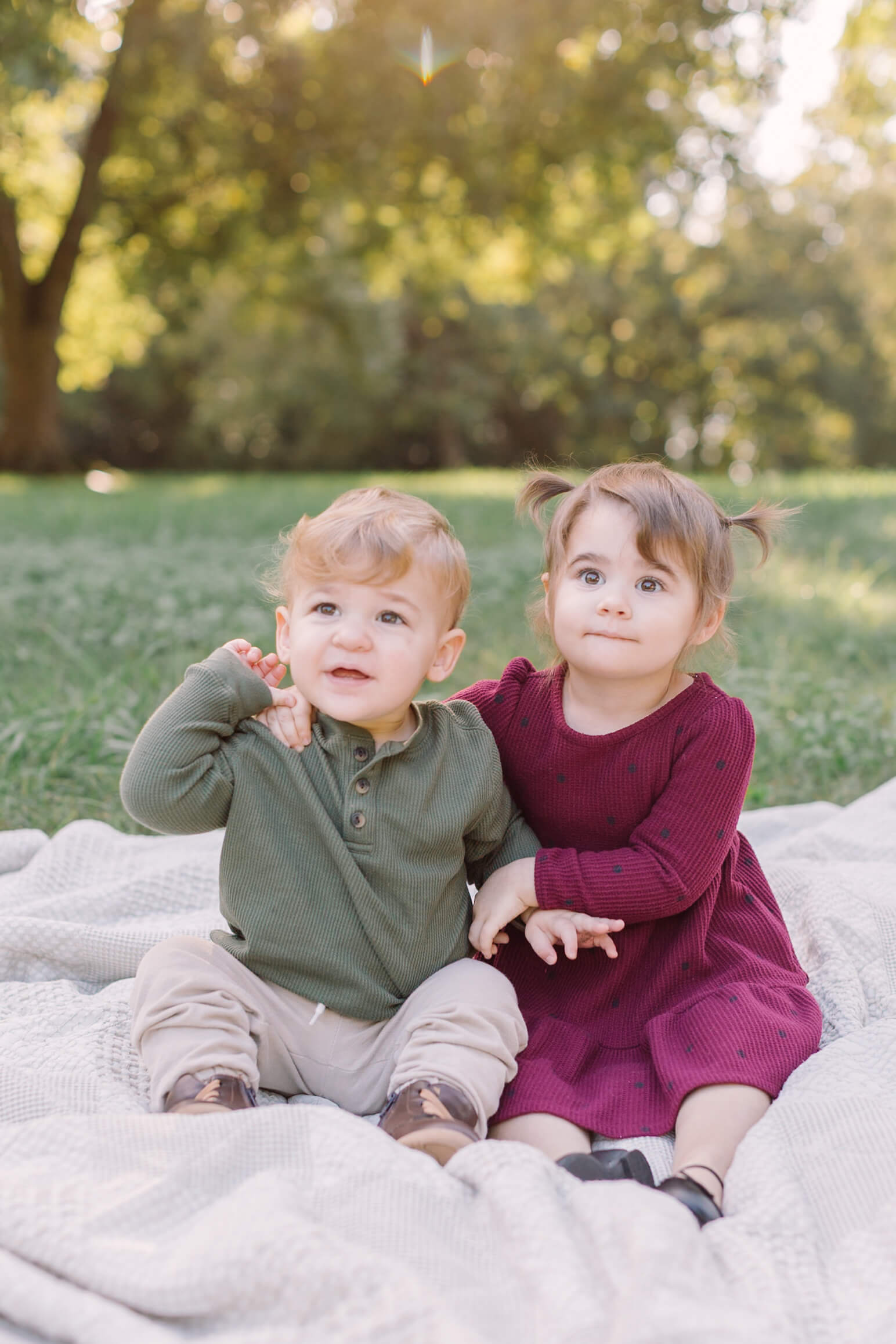 Toddler brother and sister in green and purple sit on a picnic blanket in a park lawn after some things to do in Raleigh, NC with kids