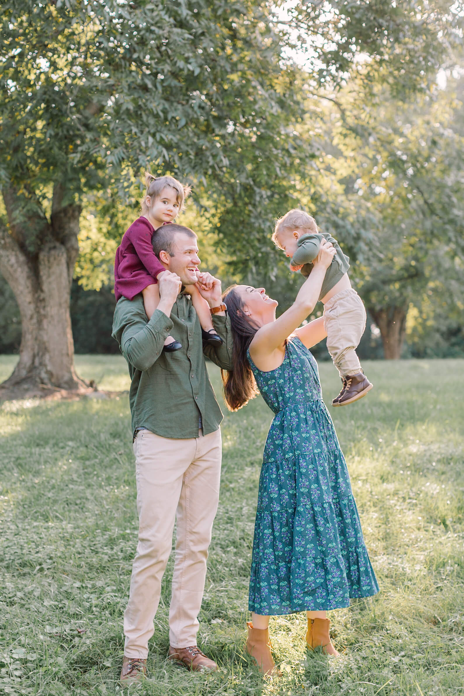 Happy mom and dad lift and hold their two toddlers in a park lawn at sunset during some things to do in Raleigh, NC with kids