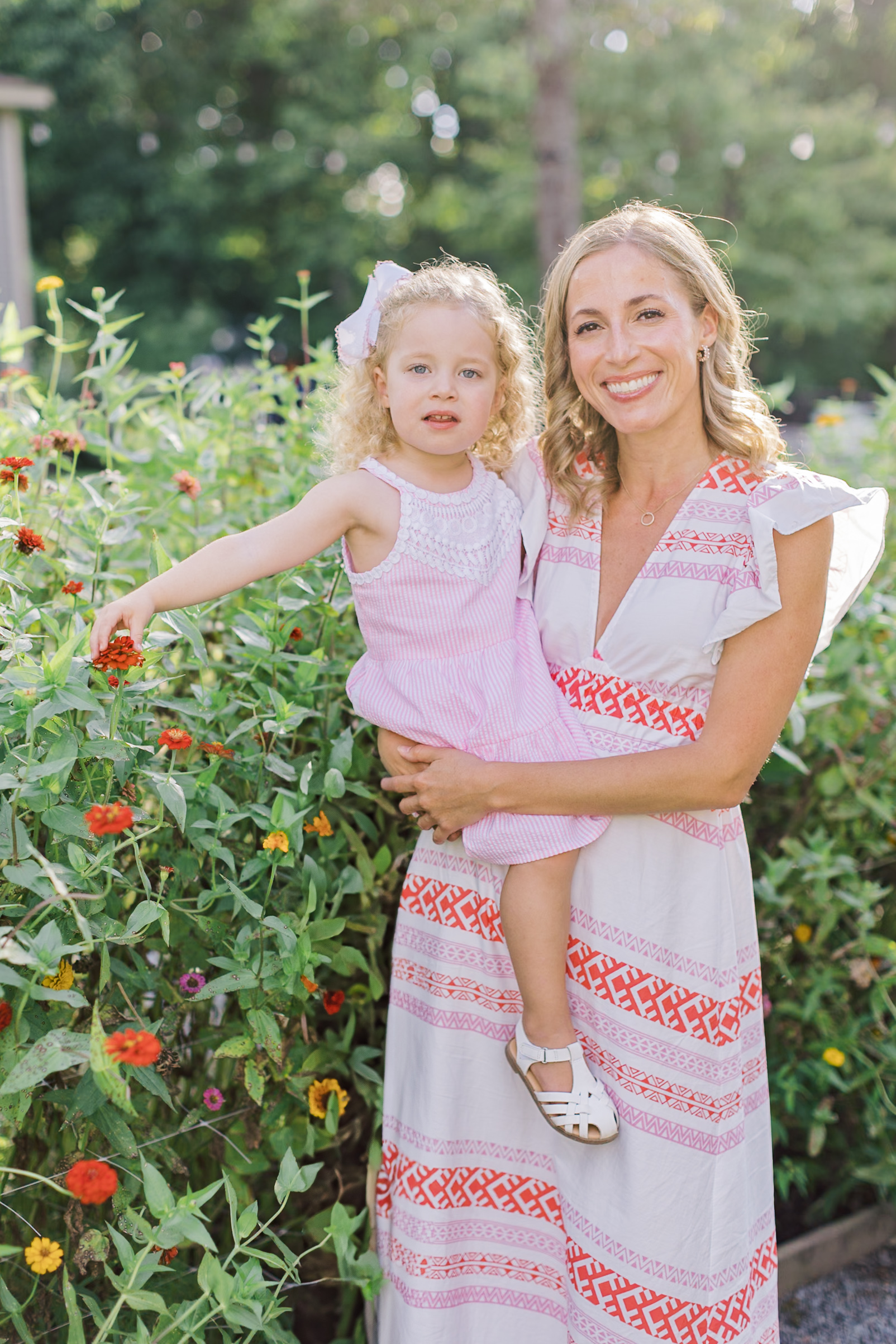 A toddler girl sits on mom's hip while standing in one of the gardens in raleigh nc at sunset
