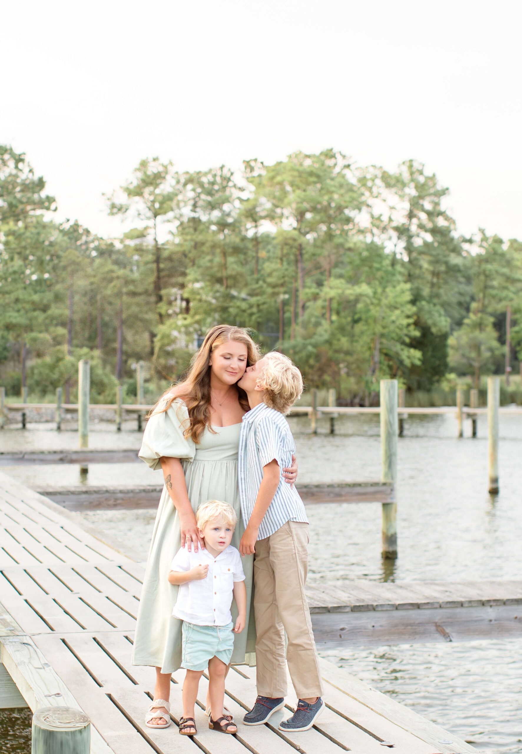 A young boy in khakis kisses his mom's cheek while standing on a boat dock at sunset after some outdoor dining in Raleigh, NC