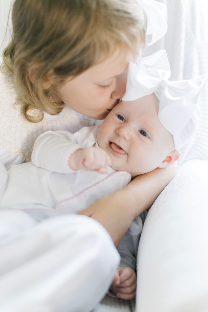 Big sister kissing her newborn baby sister during newborn photos Raleigh NC by Lindsey Lambert Photography.