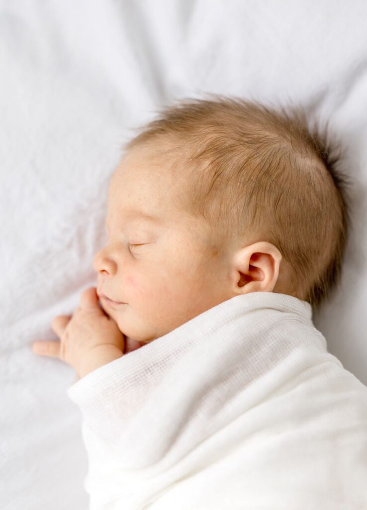 Side profile of a sleeping newborn wrapped in a white swaddle photographed by Lindsey Lambert Photography in Raleigh NC during the ideal age for newborn photos.