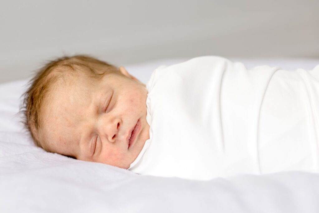 Peacefully sleeping newborn baby wrapped in white during a Raleigh NC newborn session by Lindsey Lambert Photography, showing when to take newborn photos.