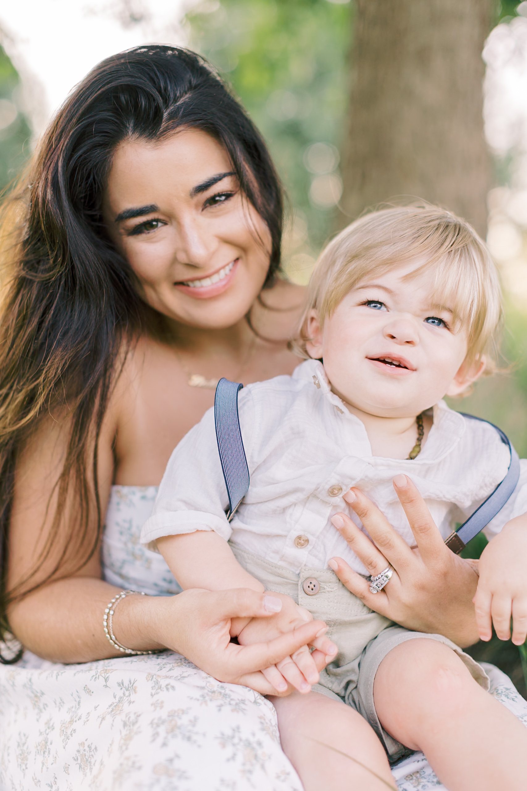 A smiling brunette mother in a floral dress holds her blonde son wearing suspenders and a white button up after their baby music classes in raleigh nc.