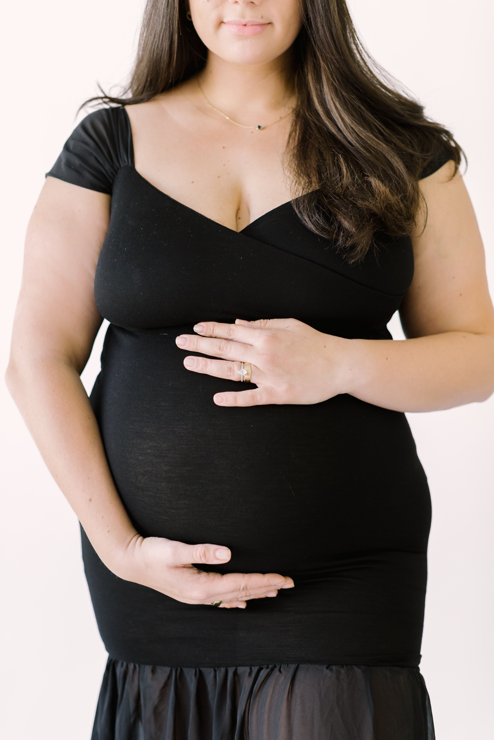 Details of a mother to be's hands on her bump in a studio in a black maternity gown thanks to fertility clinics in Raleigh, NC