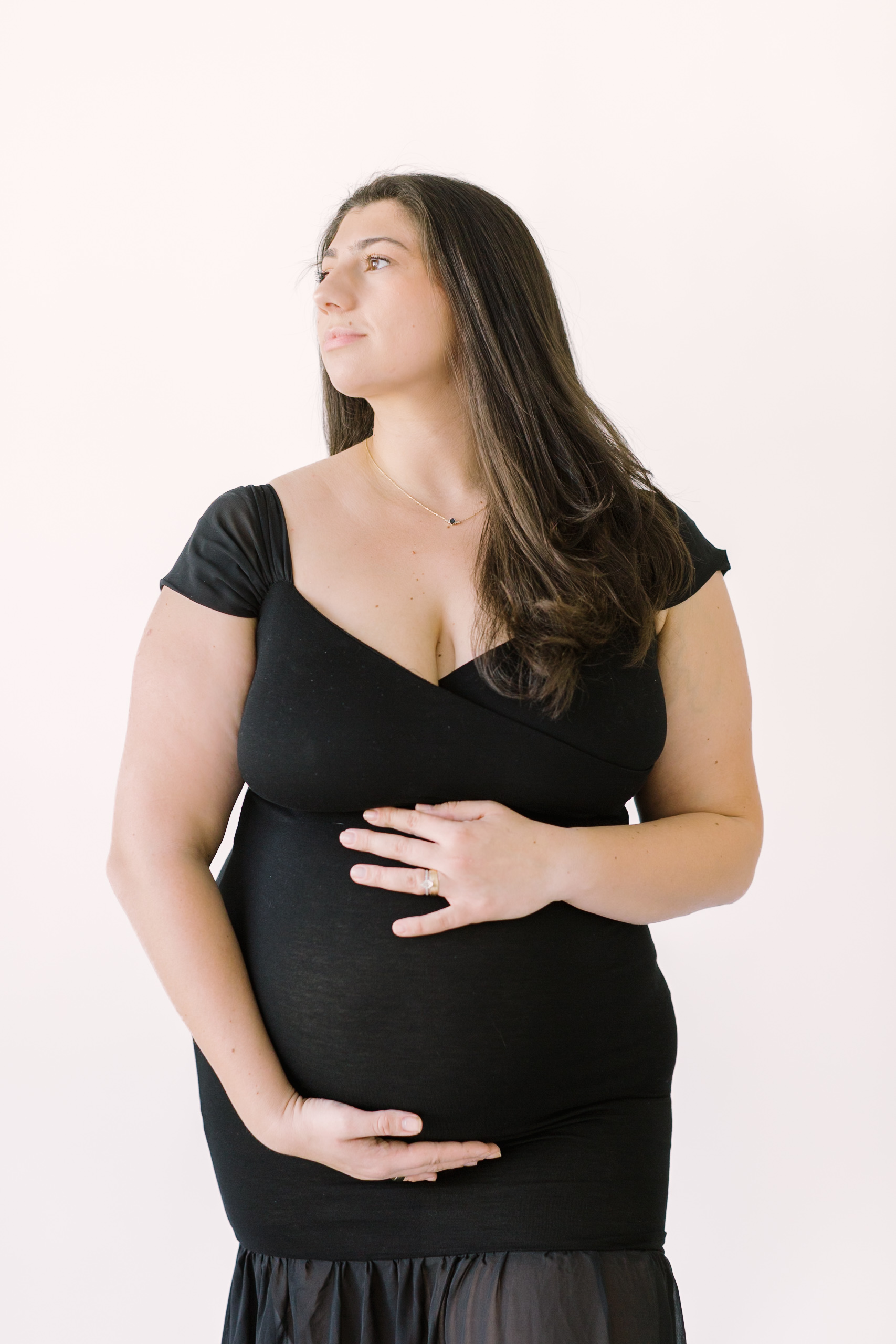 A smiling expectant woman in a black body con maternity gown smiles over her shoulder thanks to fertility clinics in Raleigh, NC