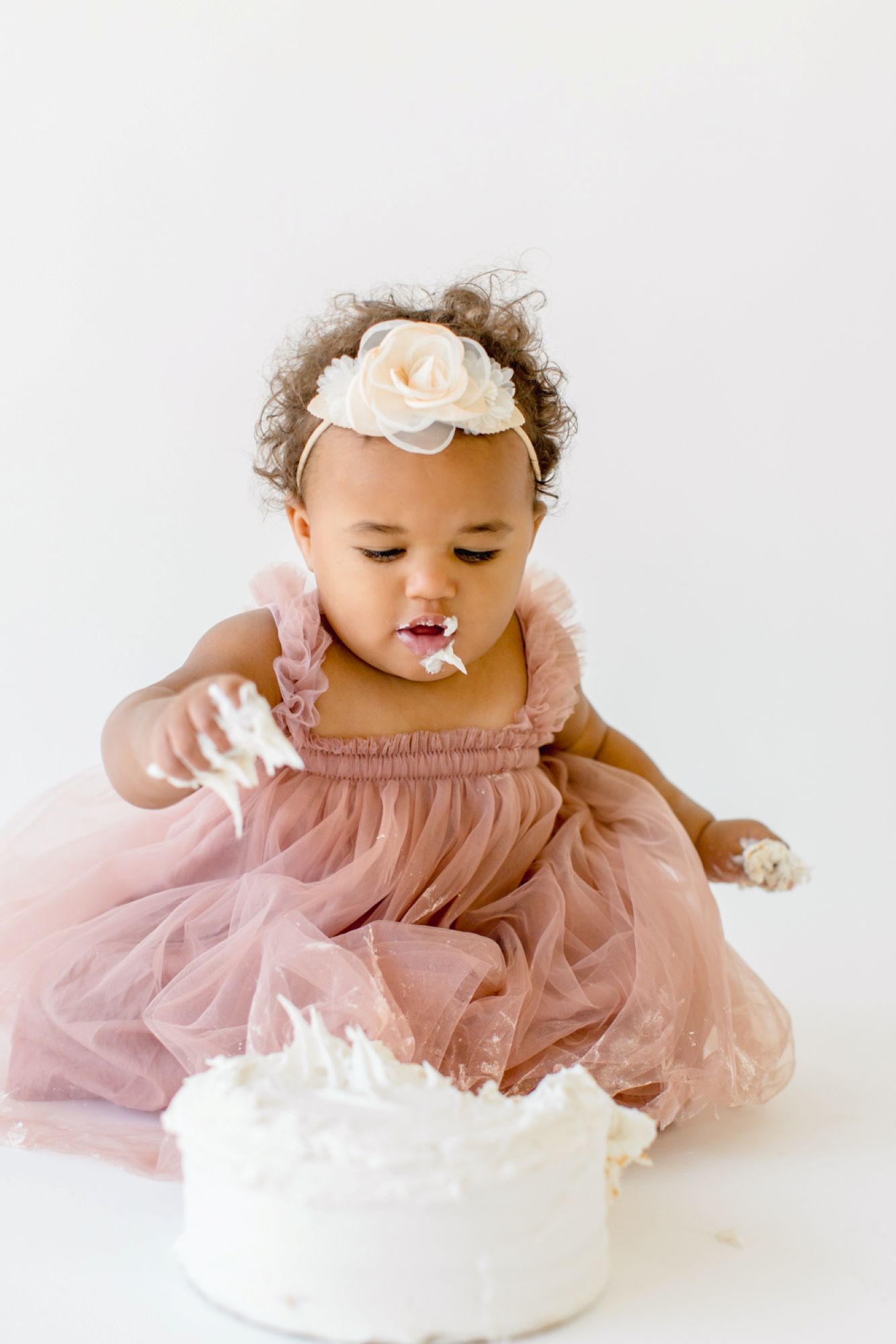 Baby girl enjoying her first birthday cake smash photoshoot in a Raleigh NC studio by Lindsey Lambert Photography.