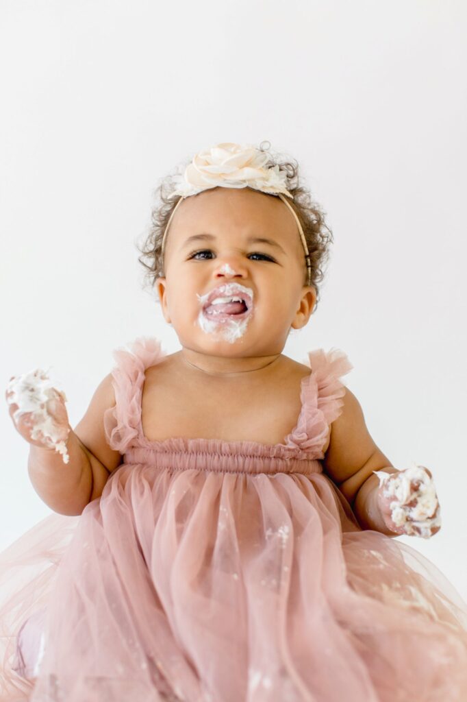 Smiling one-year-old covered in frosting during a first birthday cake smash photos session by Lindsey Lambert Photography.