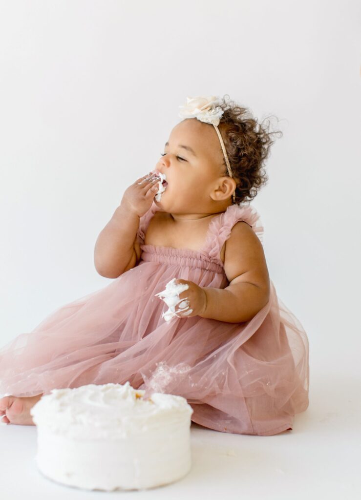 First birthday cake smash photoshoot featuring a baby girl tasting birthday cake in a light and airy Raleigh NC studio.