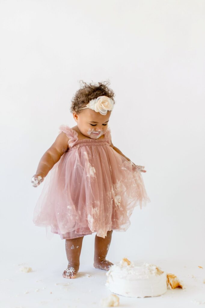 Toddler standing beside her cake during first birthday cake smash photos captured by Lindsey Lambert Photography in Raleigh NC.
