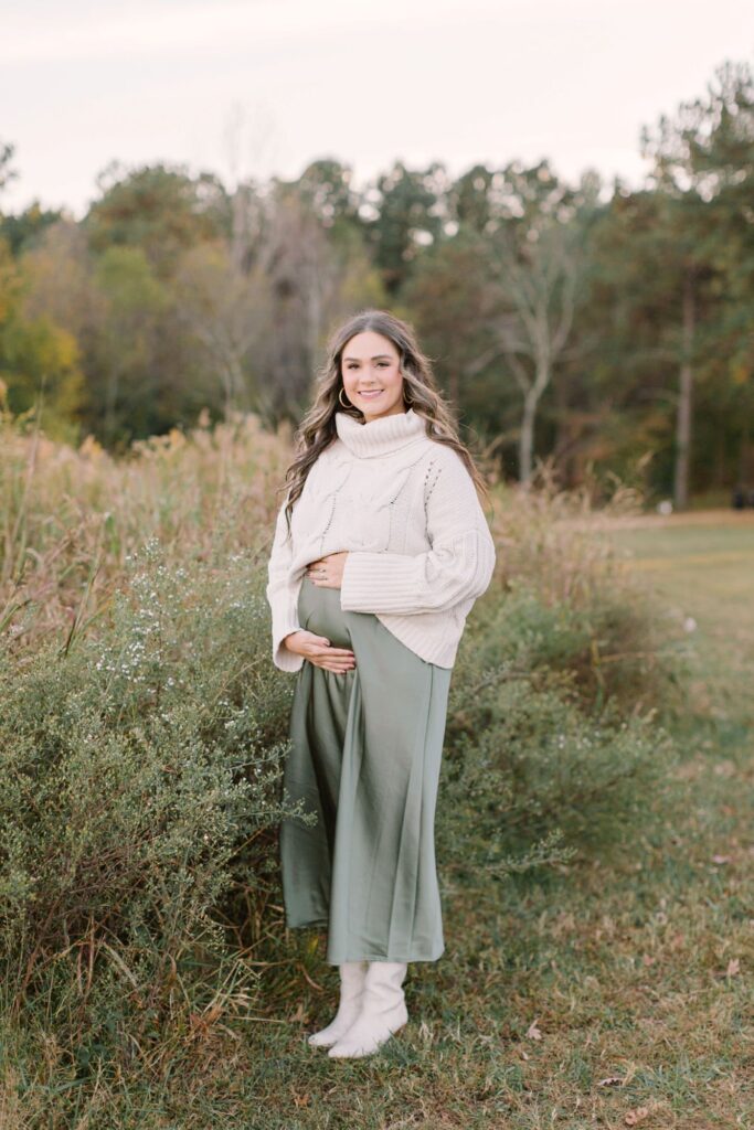 Expectant mother in a neutral sweater and olive green maxi skirt showcasing maternity photo outfit ideas for an outdoor Raleigh NC maternity session.